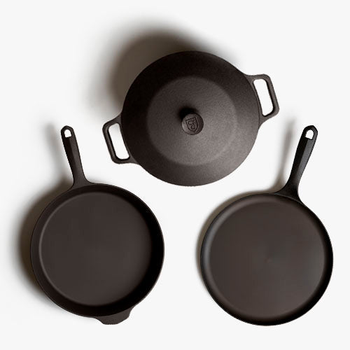 Four black cast iron skillets with loop handles and circular cooking surfaces