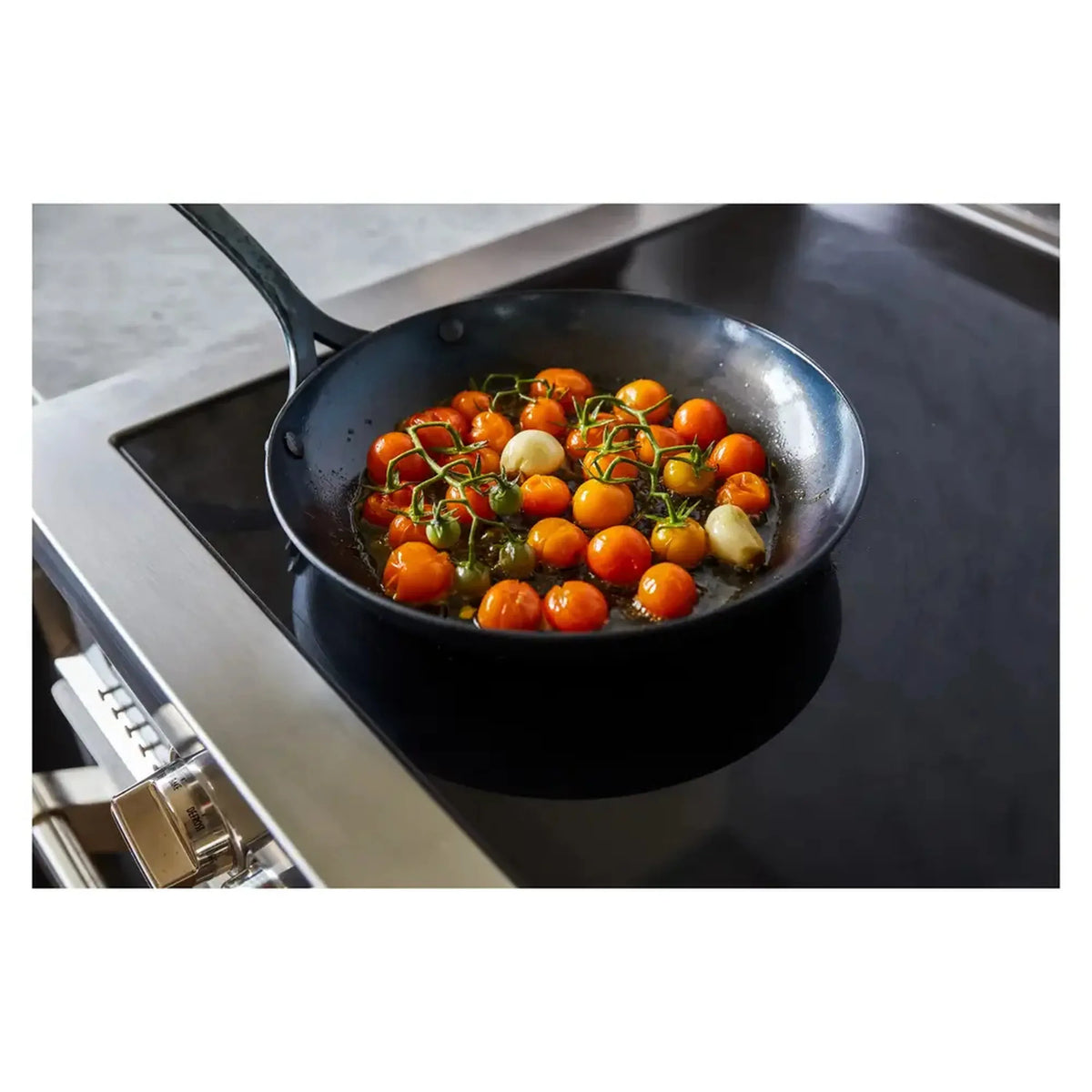 Black skillet on electric cooktop with tomatoes and herbs