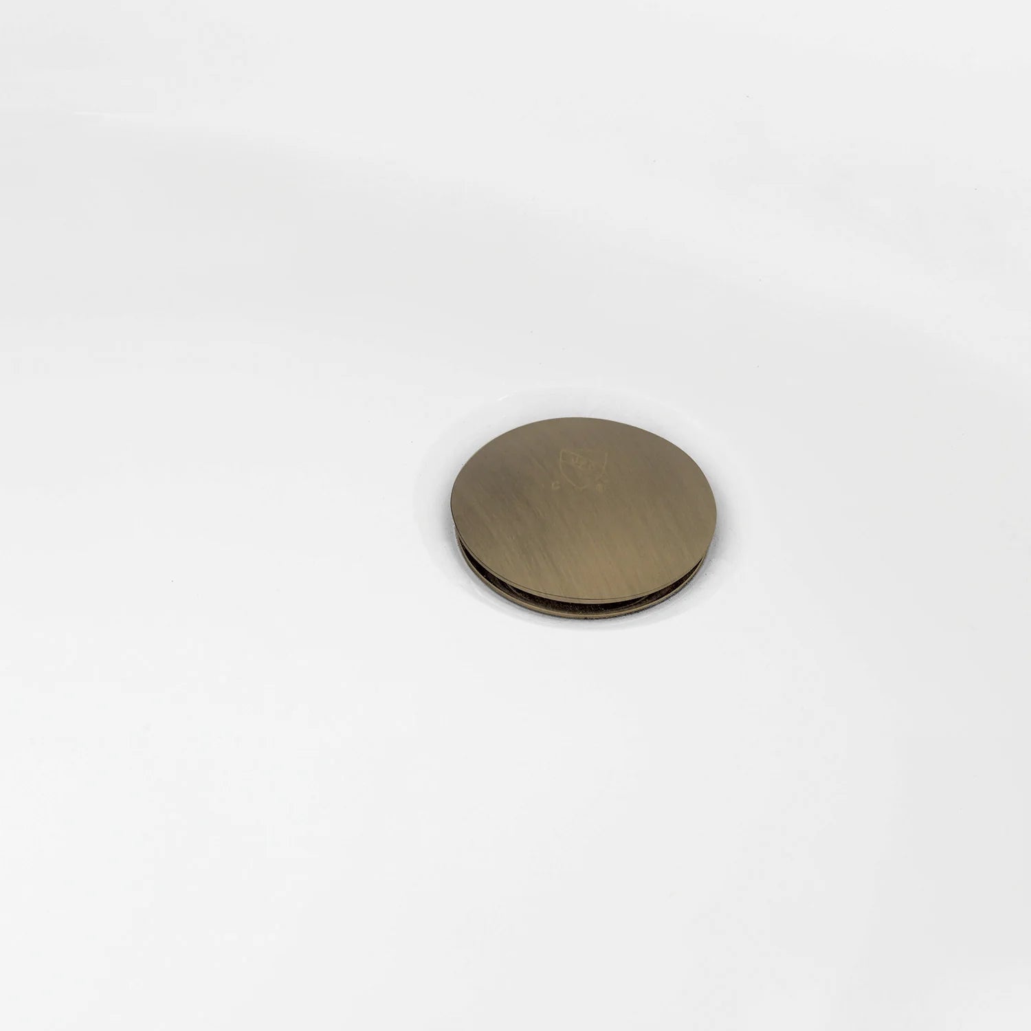 Antique brass round drain cap on white acrylic tub surface