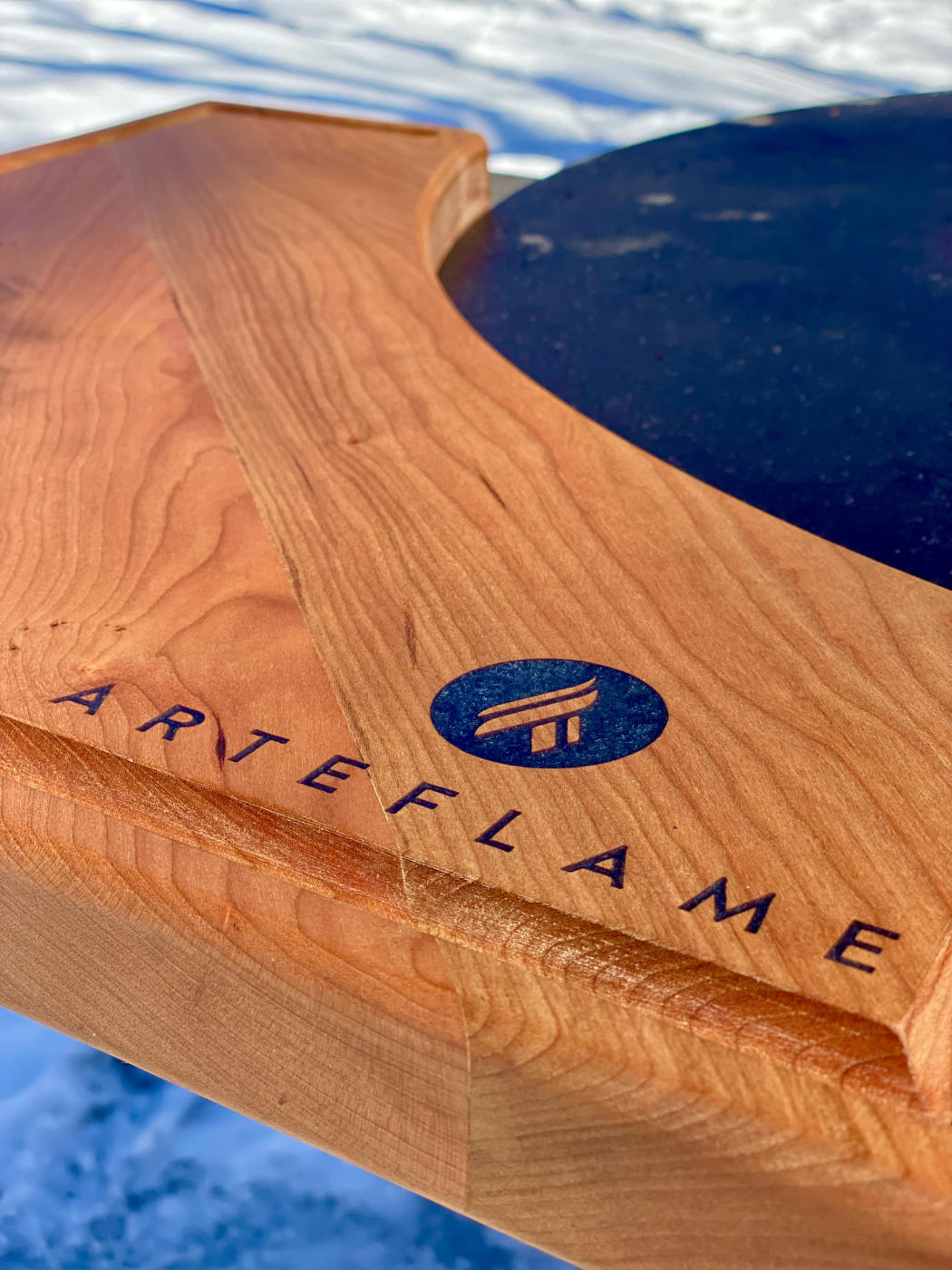 Cherry wood cutting block close-up with inlaid Arteflame logo and grain