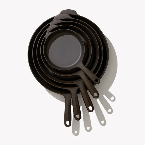 Five nested black cast iron skillets with short loop handles