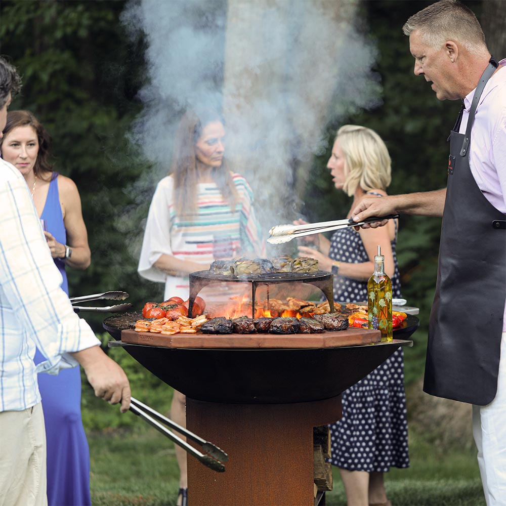 Round fire pit grill with open top and grill grate holding seared meats and vegetables