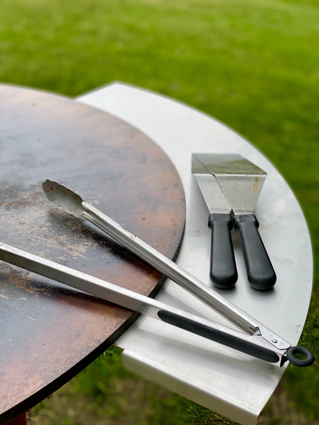 Gray round grill top with vent and grilling tools resting on edge