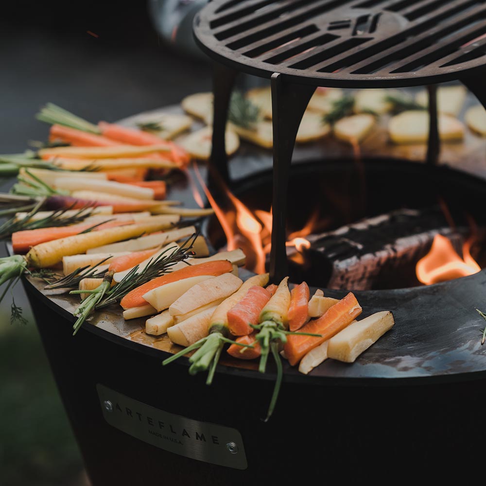 Carbon steel grill grate with sliced vegetables cooking over flames
