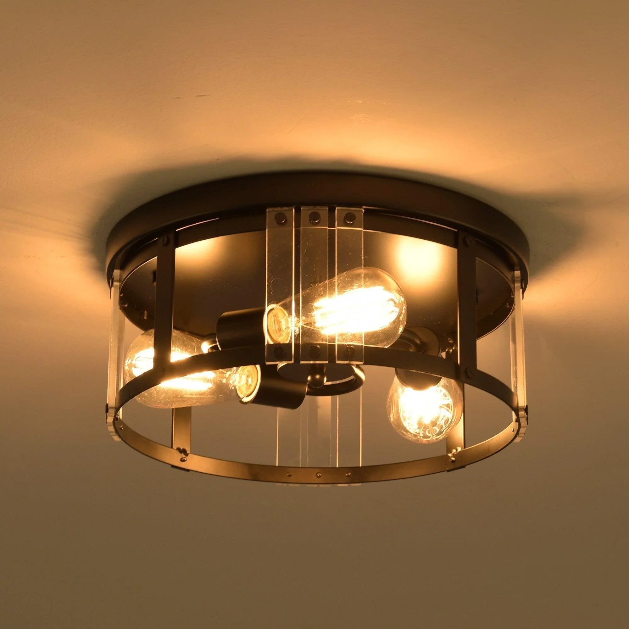 Black flush mount ceiling light with three exposed bulbs inside clear glass and metal cage