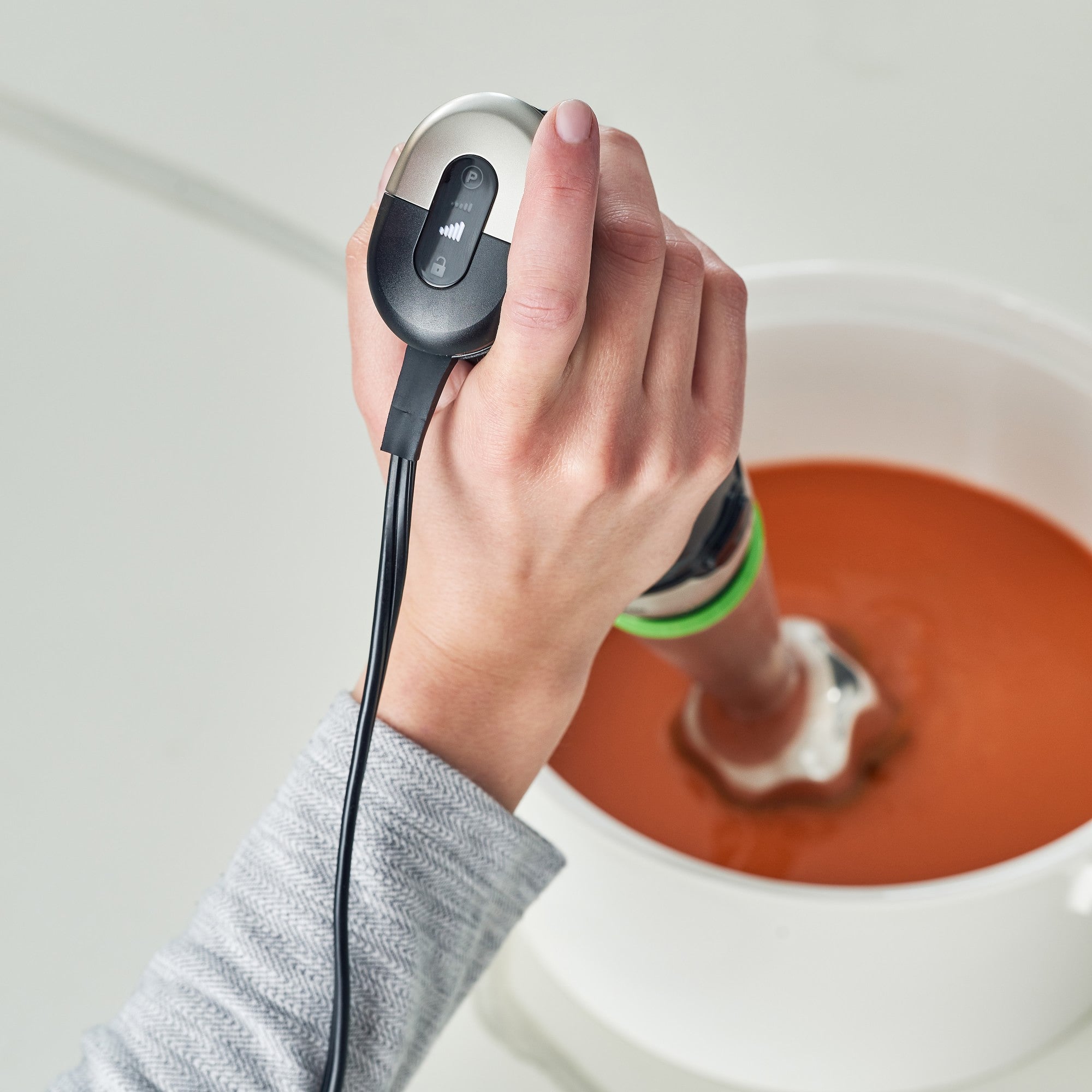 Hand holding a Braun hand blender over a mixing bowl with a blending wand attached.