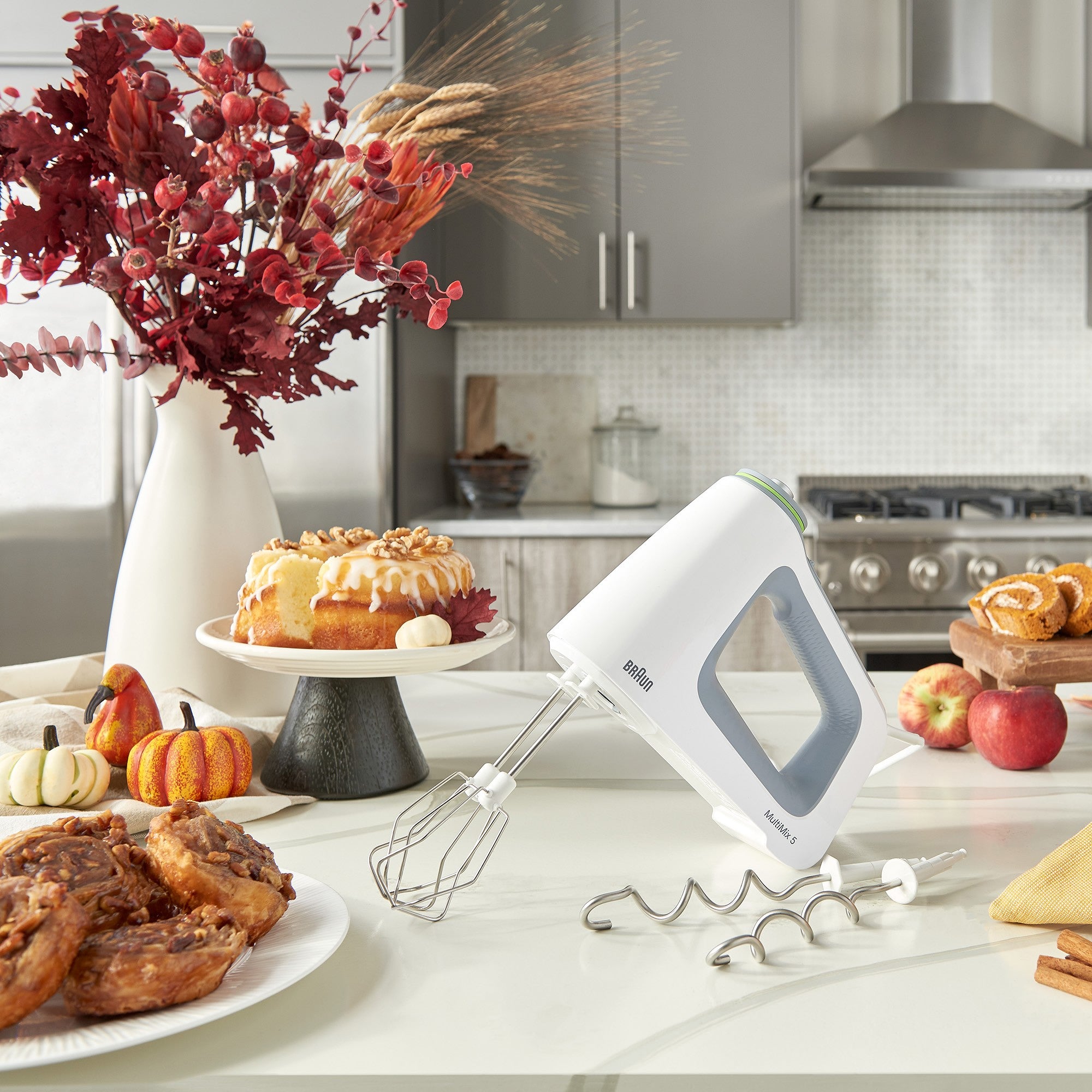 White hand mixer with beaters and dough hooks, plus mixing accessories on countertop