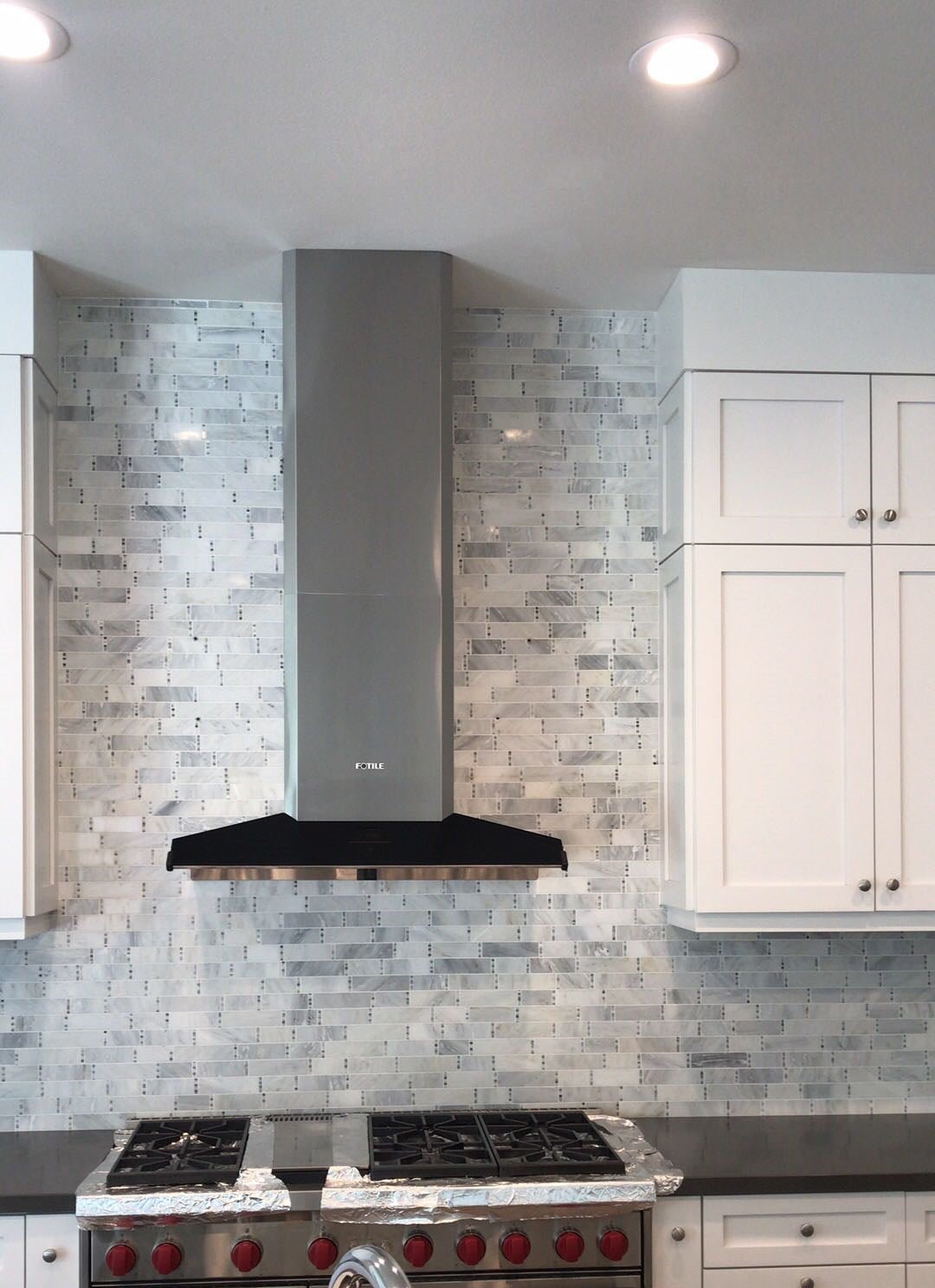 Stainless steel range hood with chimney cover against tiled backsplash