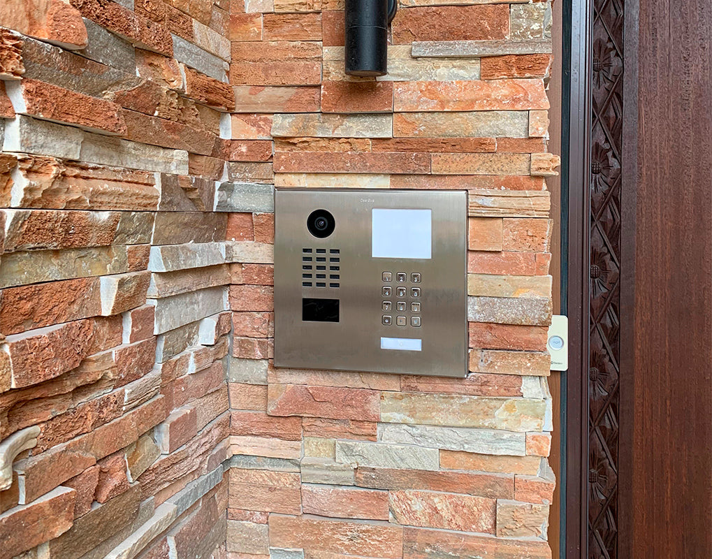 DoorBird IP video door station mounted on brick wall with keypad and camera window