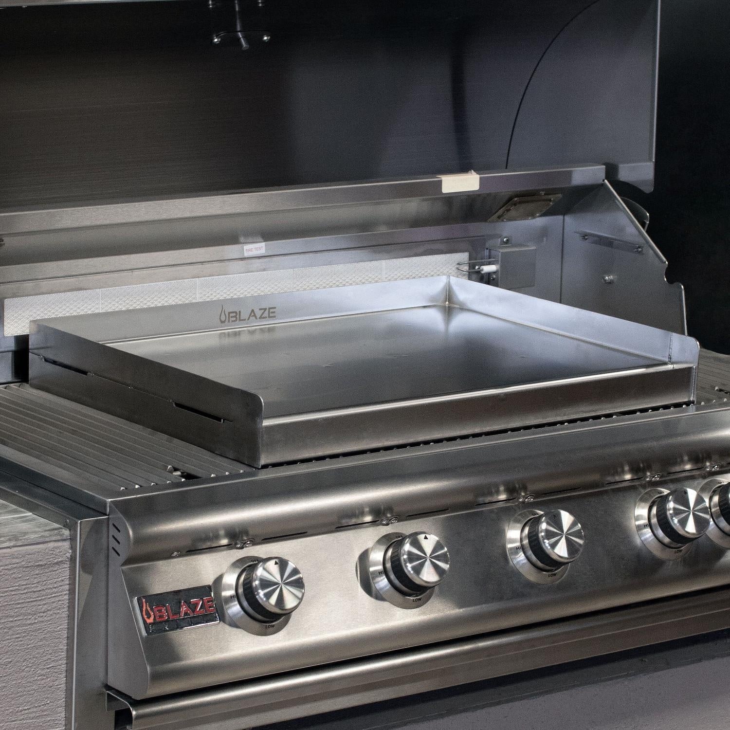 Stainless griddle plate fitted on outdoor grill, with front control knobs visible