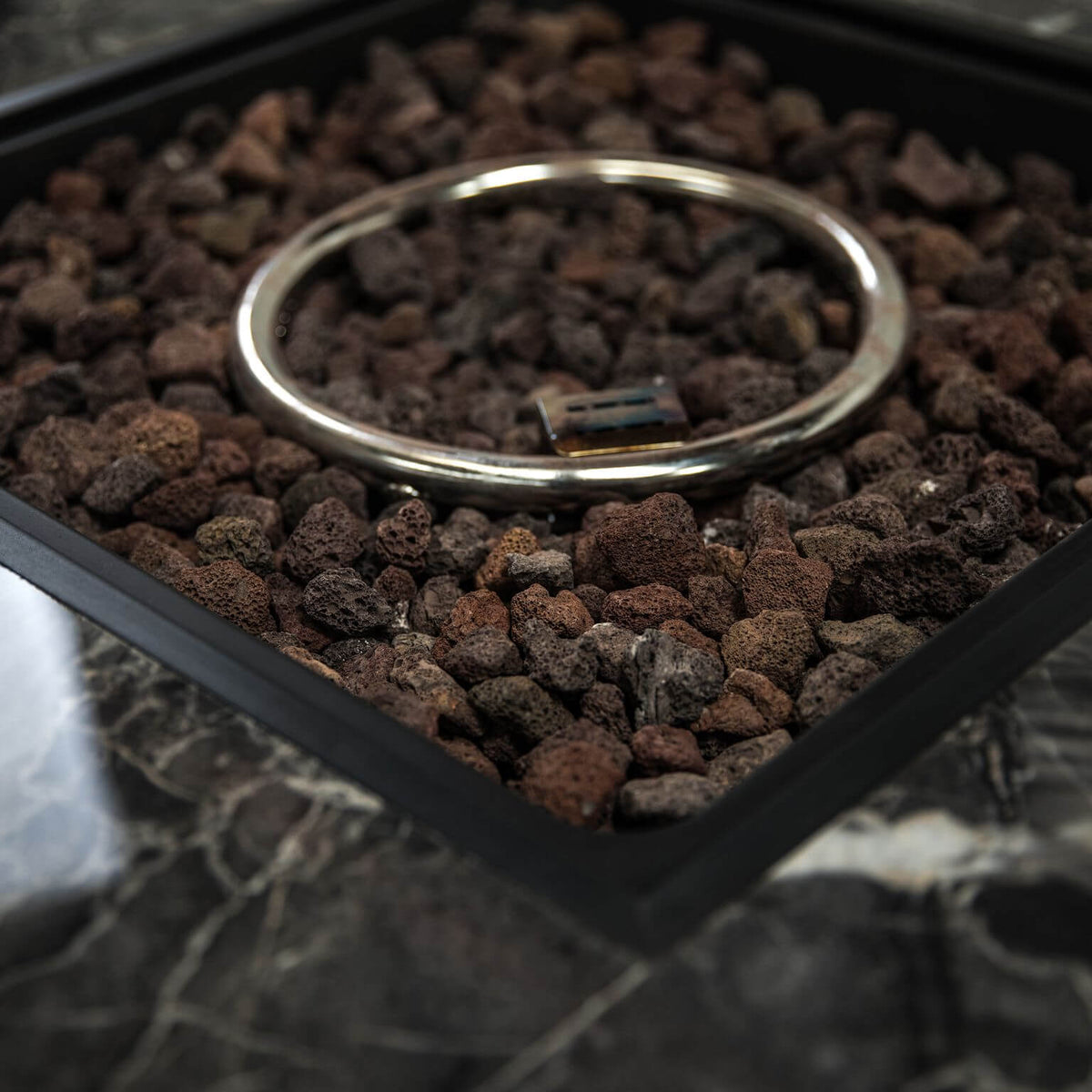 Square fire bowl filled with brown lava rocks and a metal ring handle on the gray top