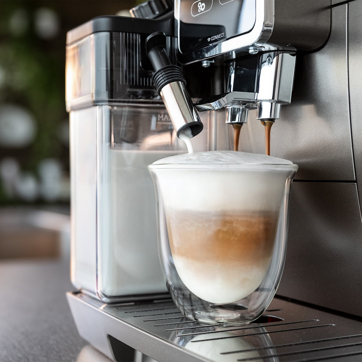 Super-automatic espresso machine dispensing coffee into a glass cup under the spouts