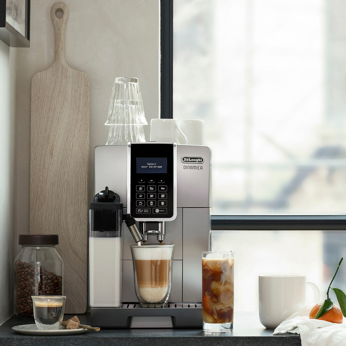 Silver espresso machine with frothing carafe and cup of latte on counter