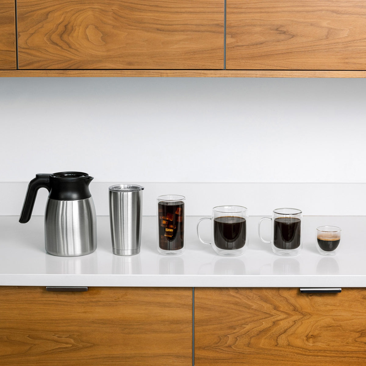 Thermal carafe and coffee cups on a counter with coffee maker base in background