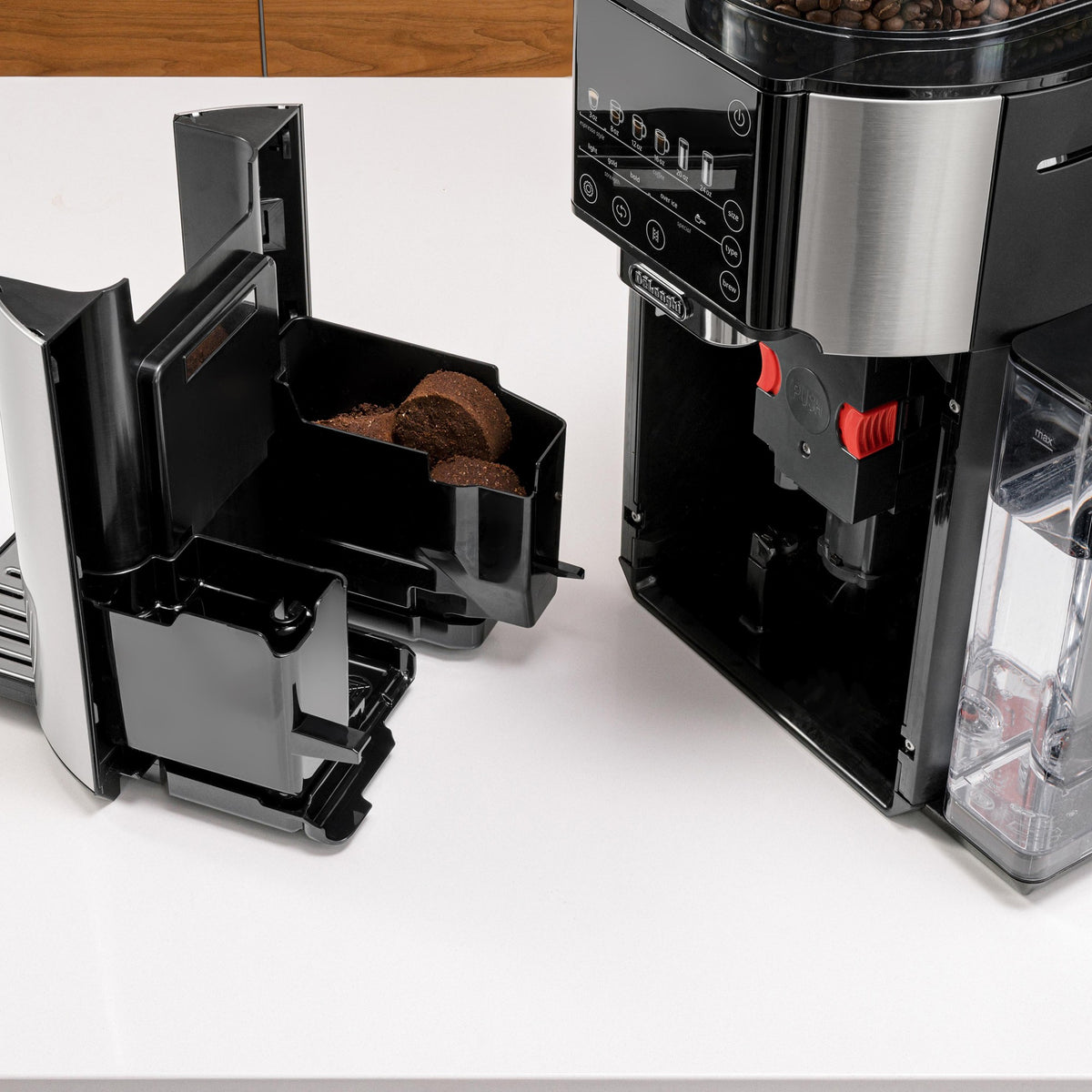 Automatic coffee maker with open bean chute and grinder chamber showing coffee grounds