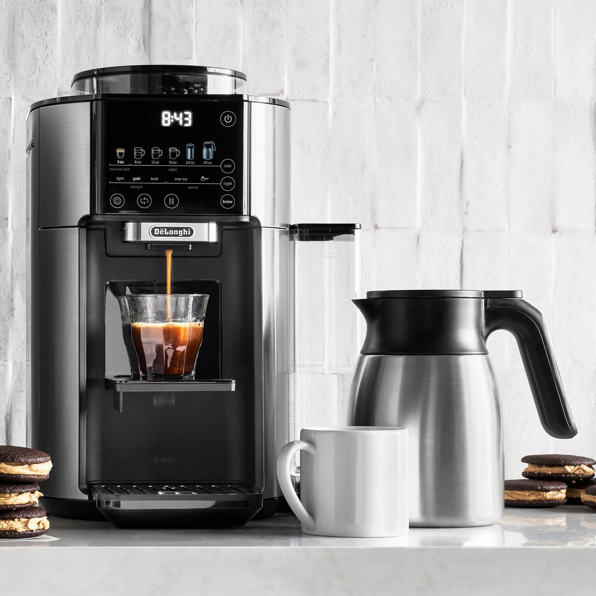 Automatic coffee maker dispensing coffee into a glass cup beside a stainless thermal carafe