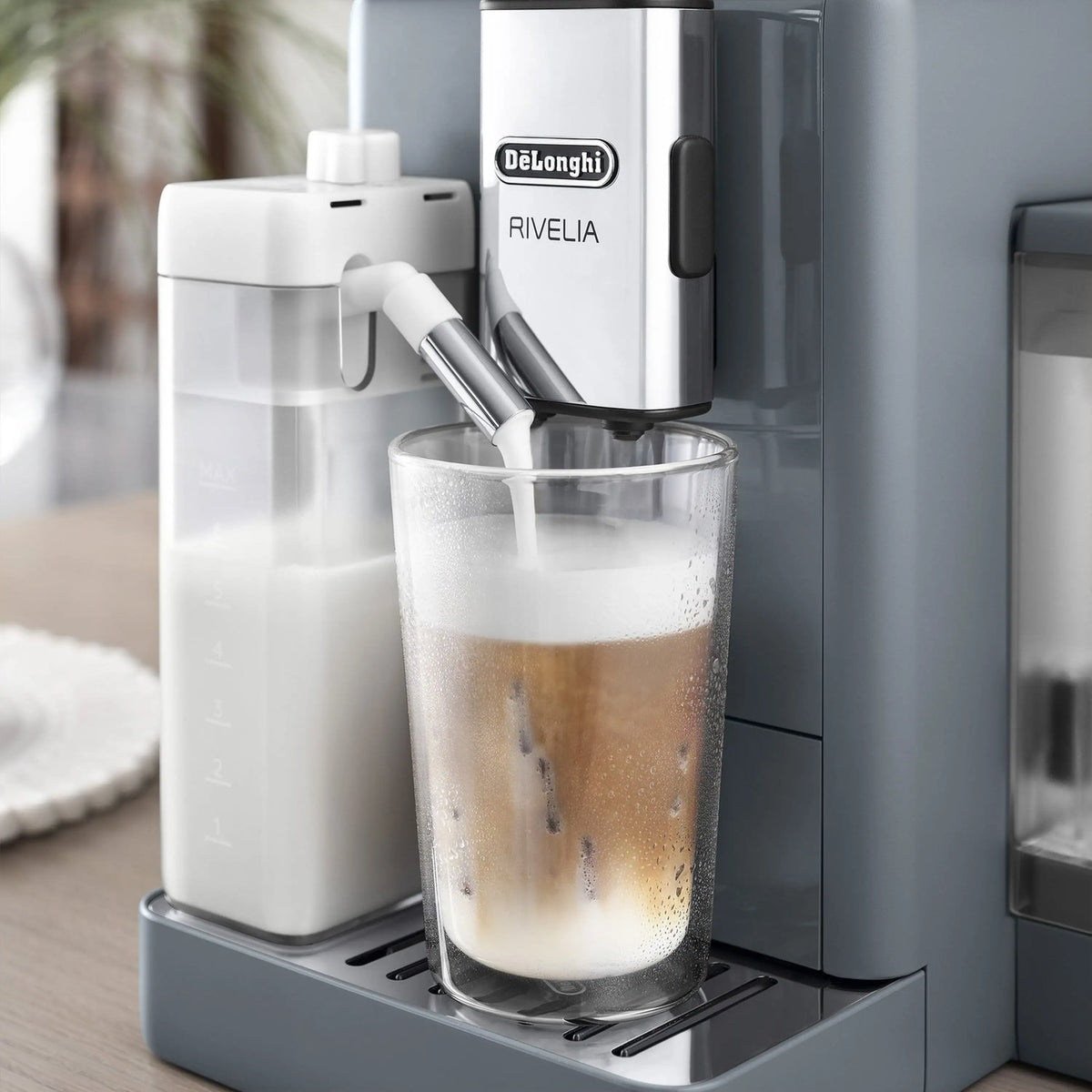 Cold milk frother accessory with white reservoir and spout, dispensing foam into a glass
