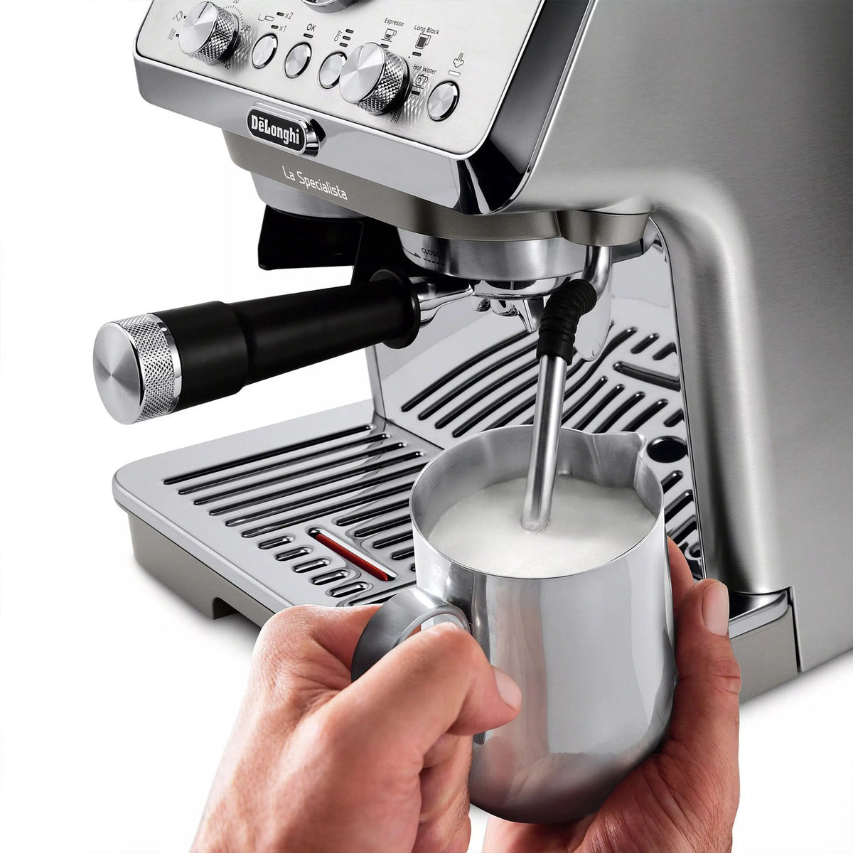 Hands holding metal milk jug under spout of stainless espresso machine.