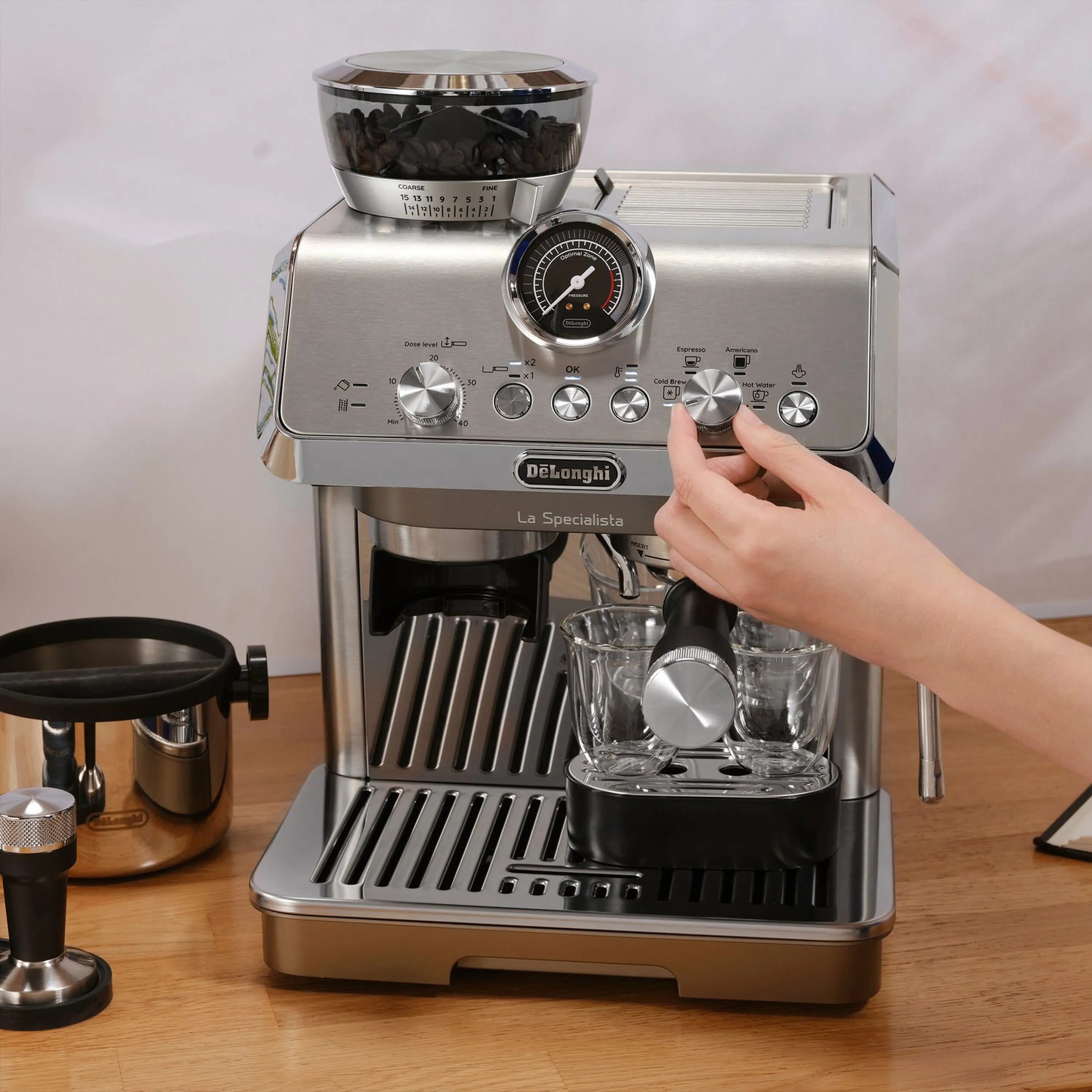 Stainless espresso machine with hand on front controls and frothing spout detail.