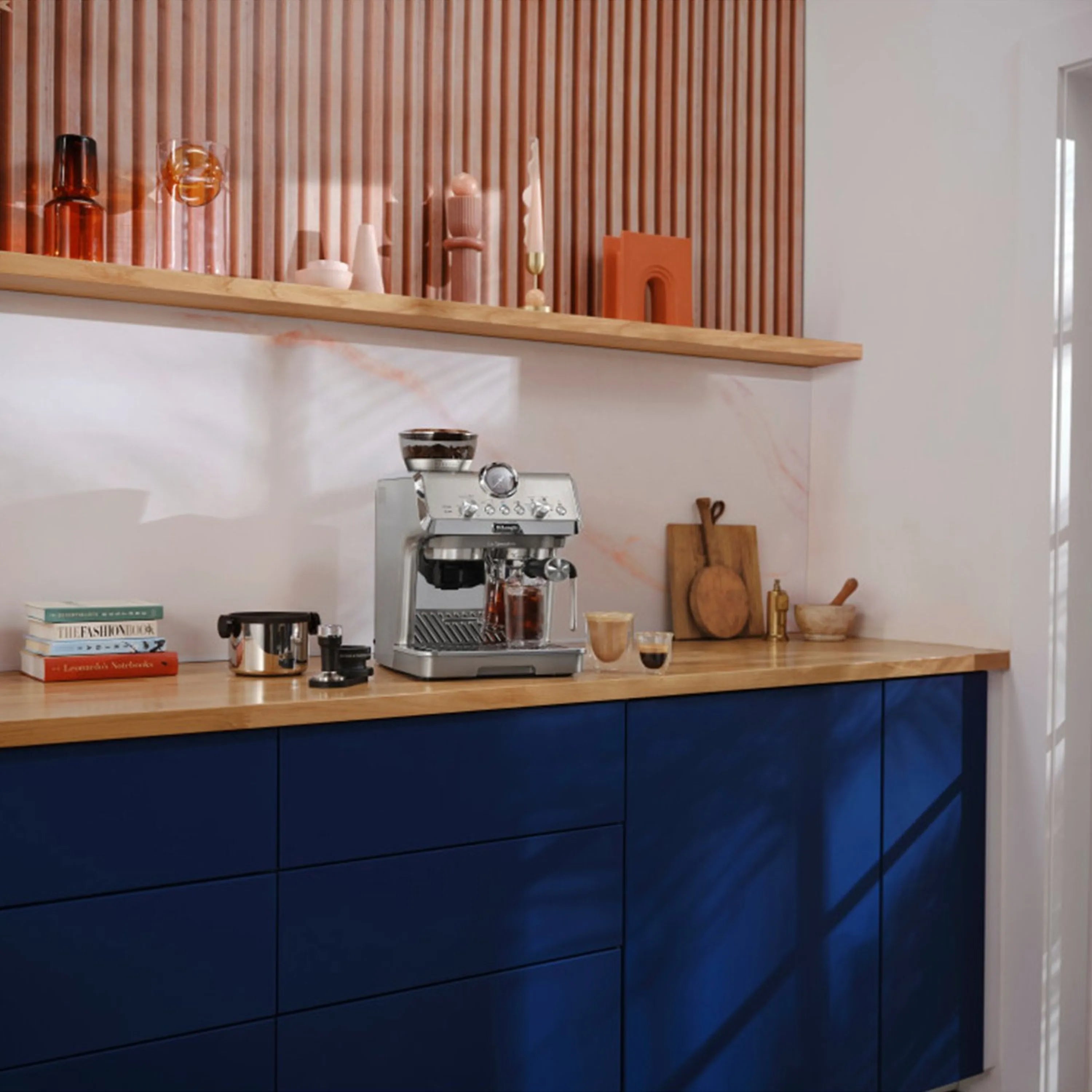 Stainless espresso machine on blue cabinet counter, with cold brew cup on the shelf.