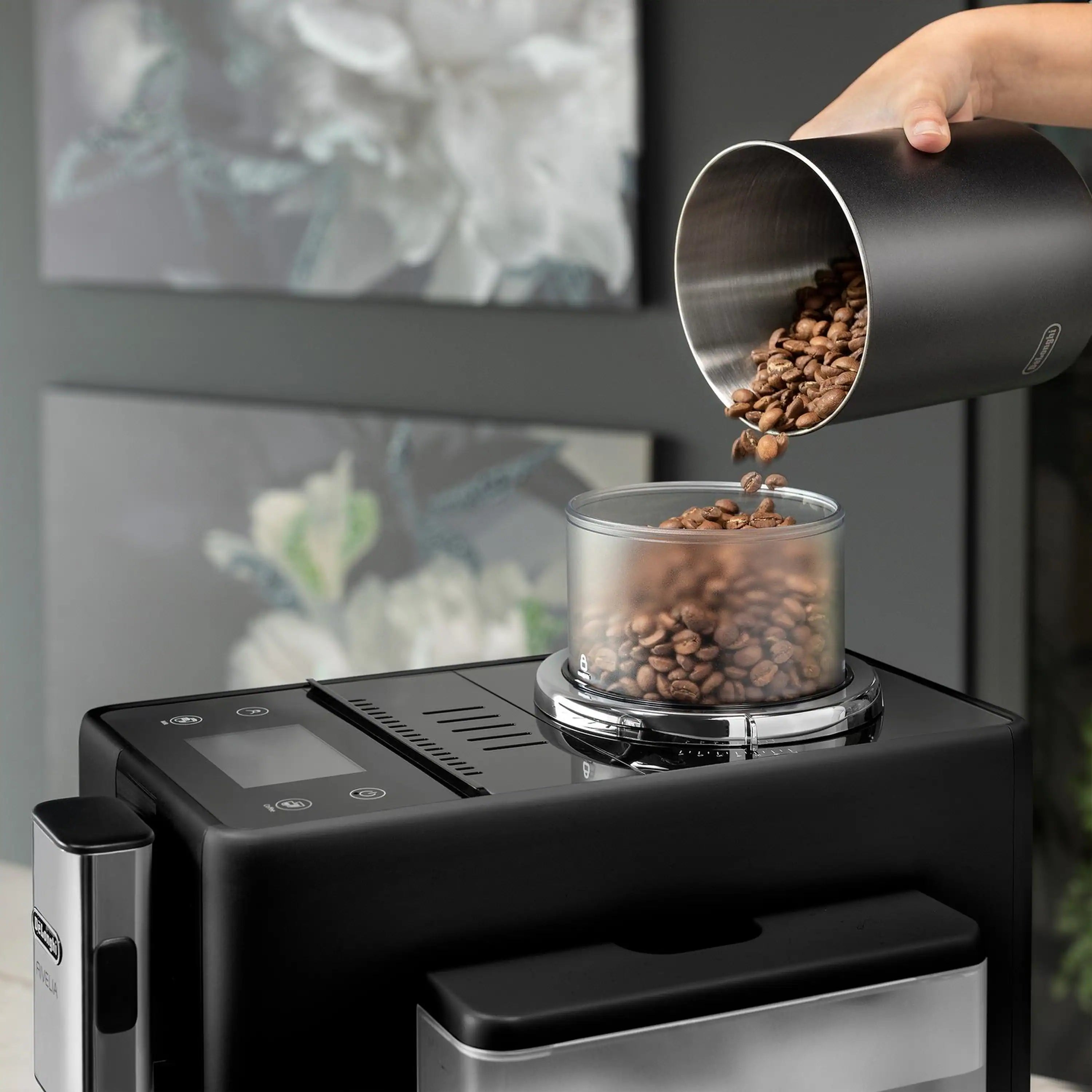 Black espresso machine with bean hopper pouring roasted coffee beans into grinder chamber