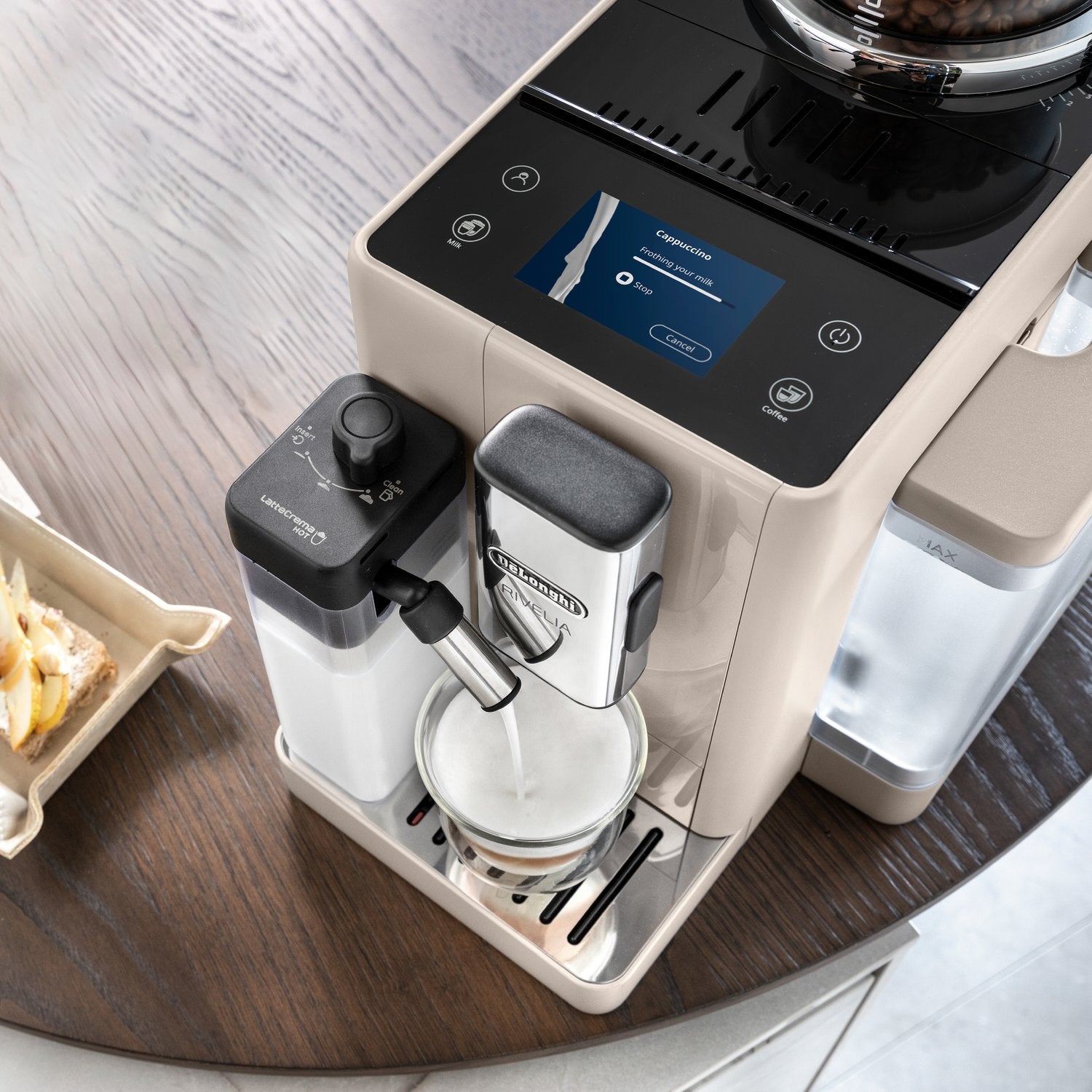 Beige espresso machine with steam wand, brewing cup on drip tray, and water container