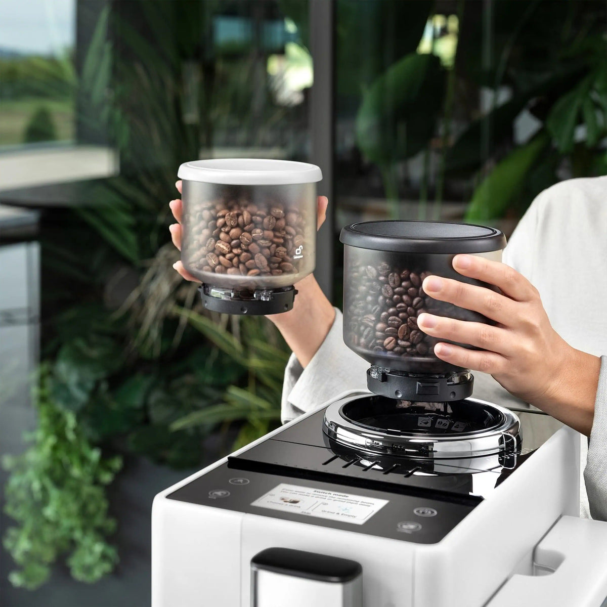 White espresso machine with two bean canisters being held above the top hopper area