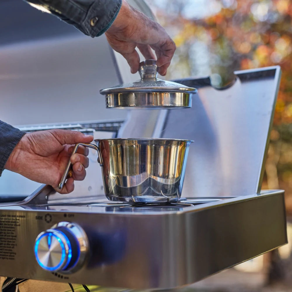 Hands placing pot on stainless propane grill grate near control knobs