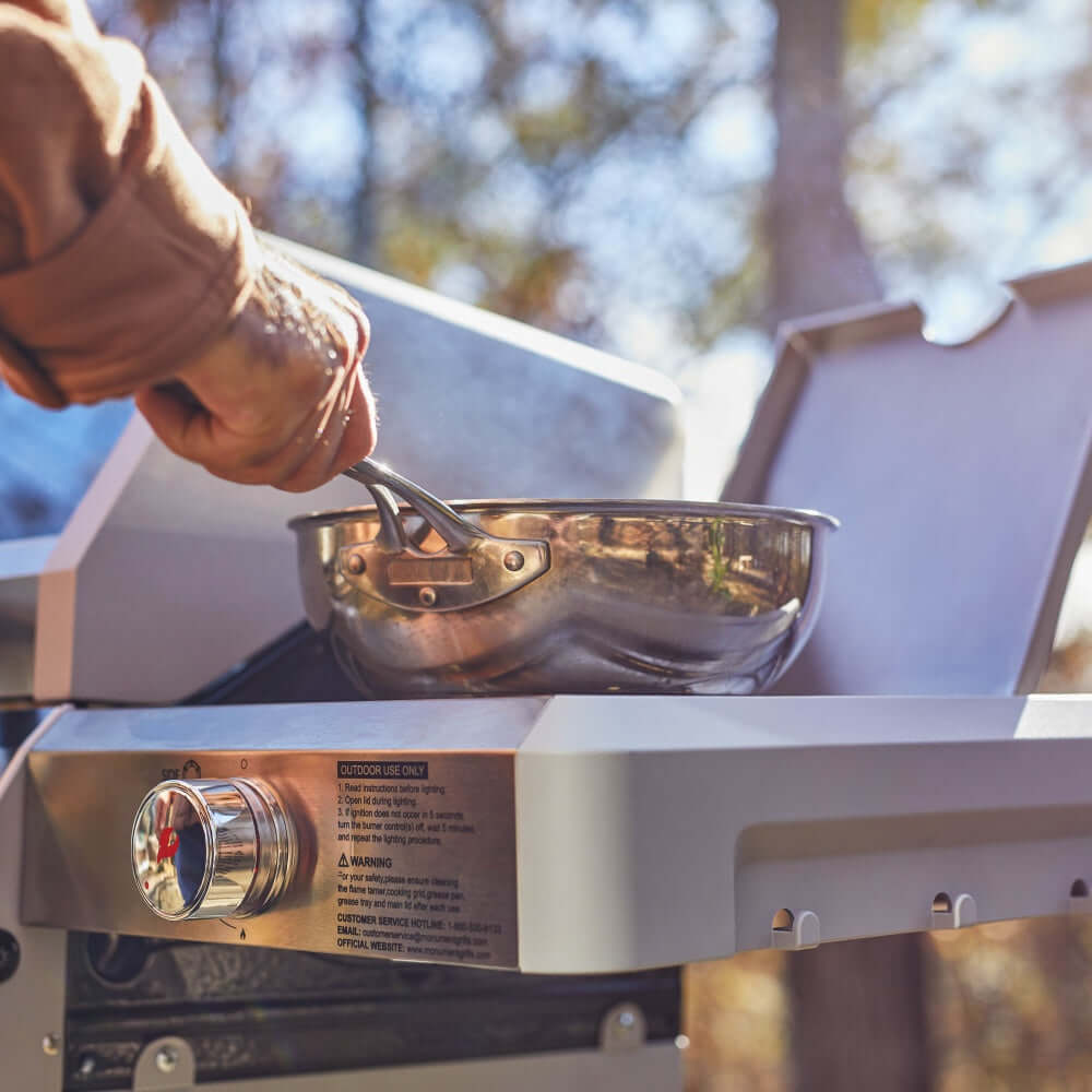 Stainless steel grill with a pot on the grate and flame hood open