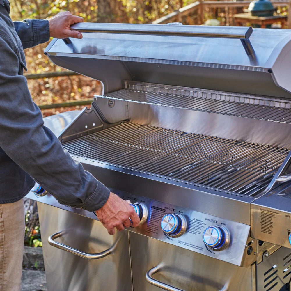 Stainless steel propane gas grill lid open showing cooking grates and control knobs