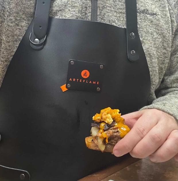 Black leather grill apron with logo patch, wide neck straps, and metal grommets