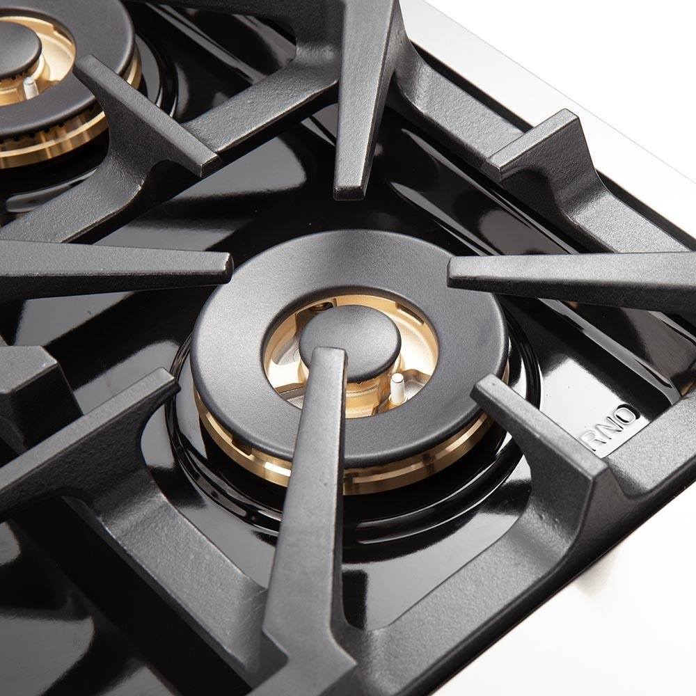 Gas range burner with black grate and brass-trimmed cap in stainless cooktop