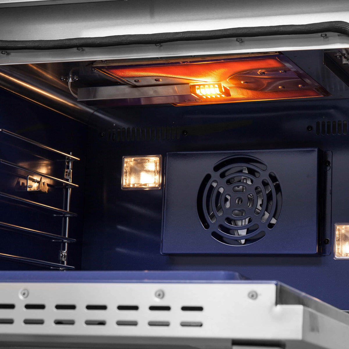 Open stainless steel gas oven interior with glowing light and fan vent panel