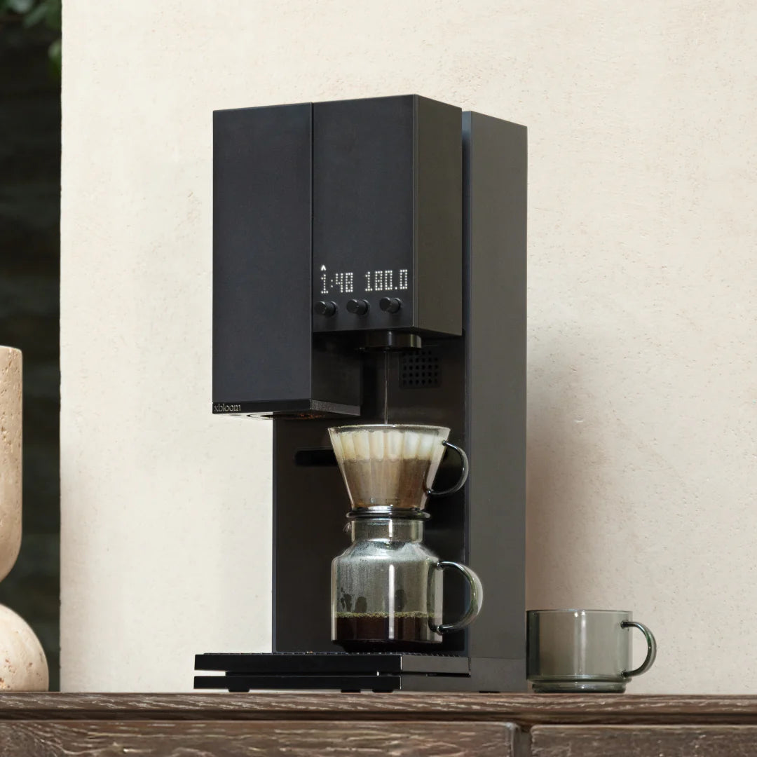 Black coffee brewer with glass filter dripper and metal server on a counter