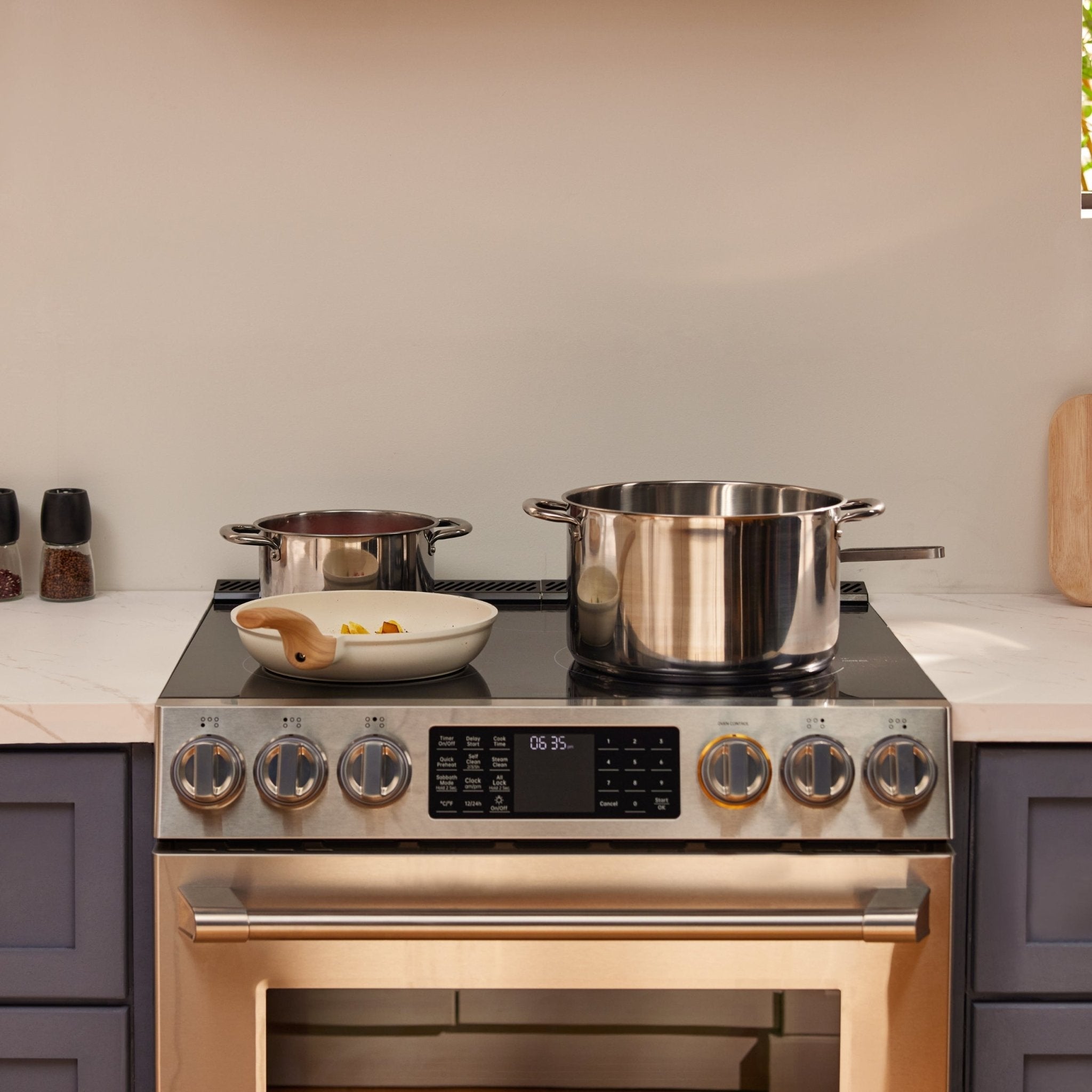 Stainless steel electric slide-in range cooktop with control knobs and cookware on top
