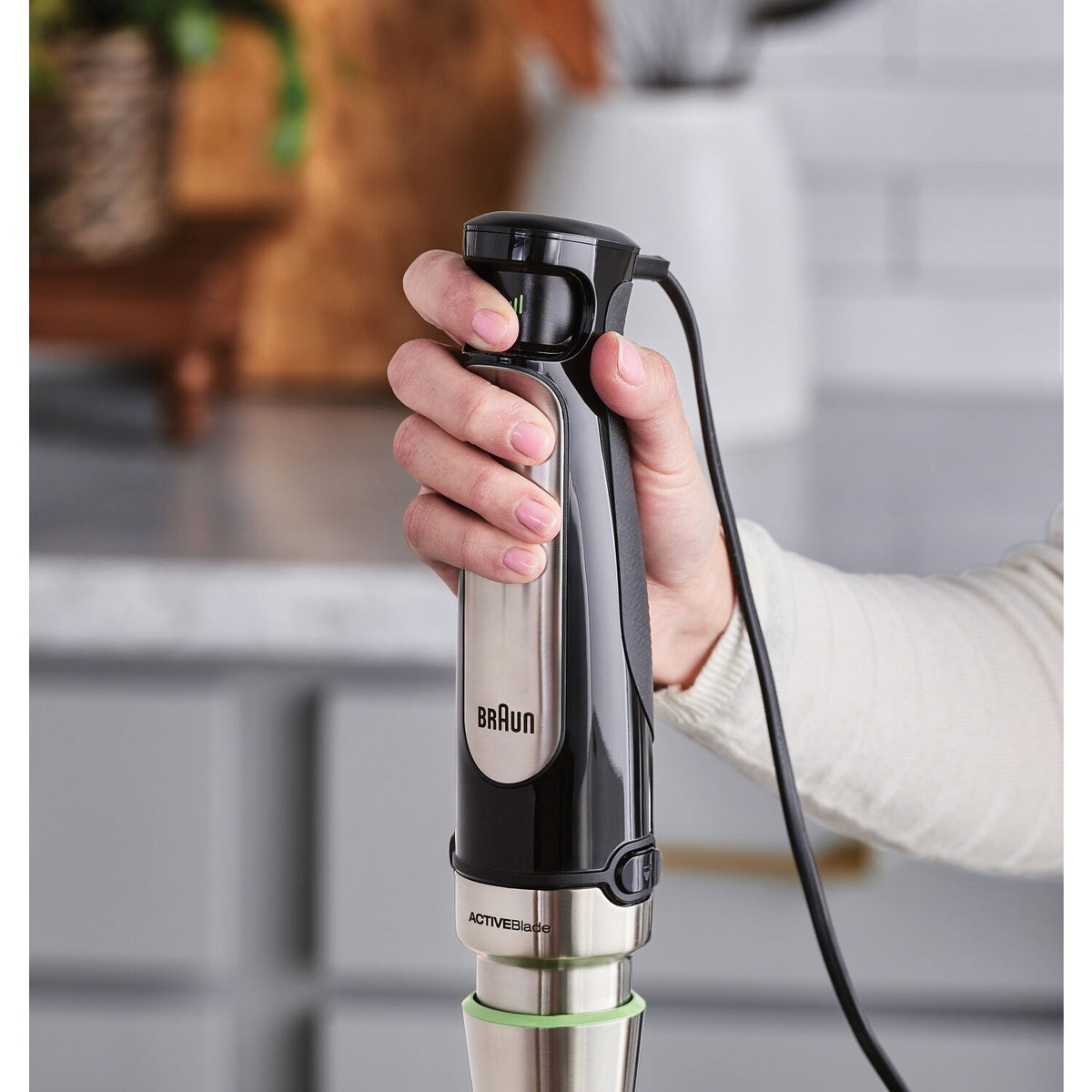 Braun stainless steel hand blender with black handle, held in a person’s hand