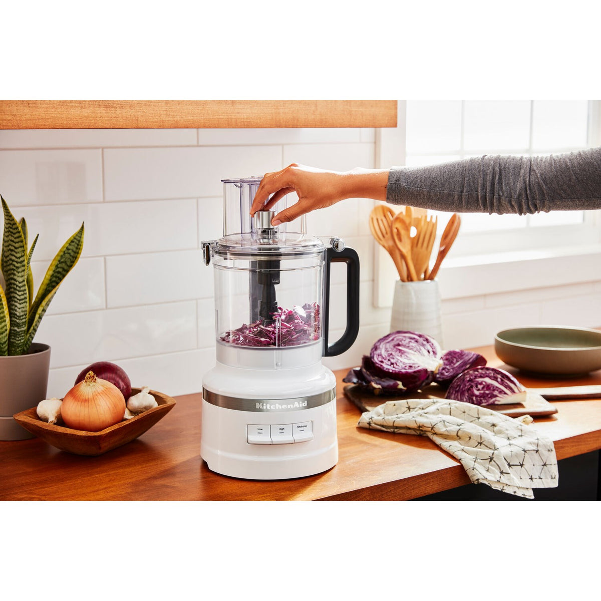 White KitchenAid food processor with transparent bowl and black handle, actively chopping