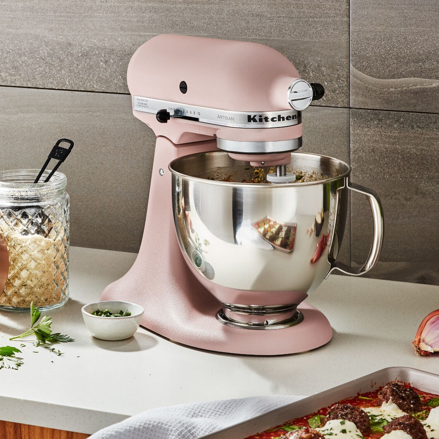 Peach tilt-head stand mixer with stainless bowl on countertop; bowl reflects ingredients.