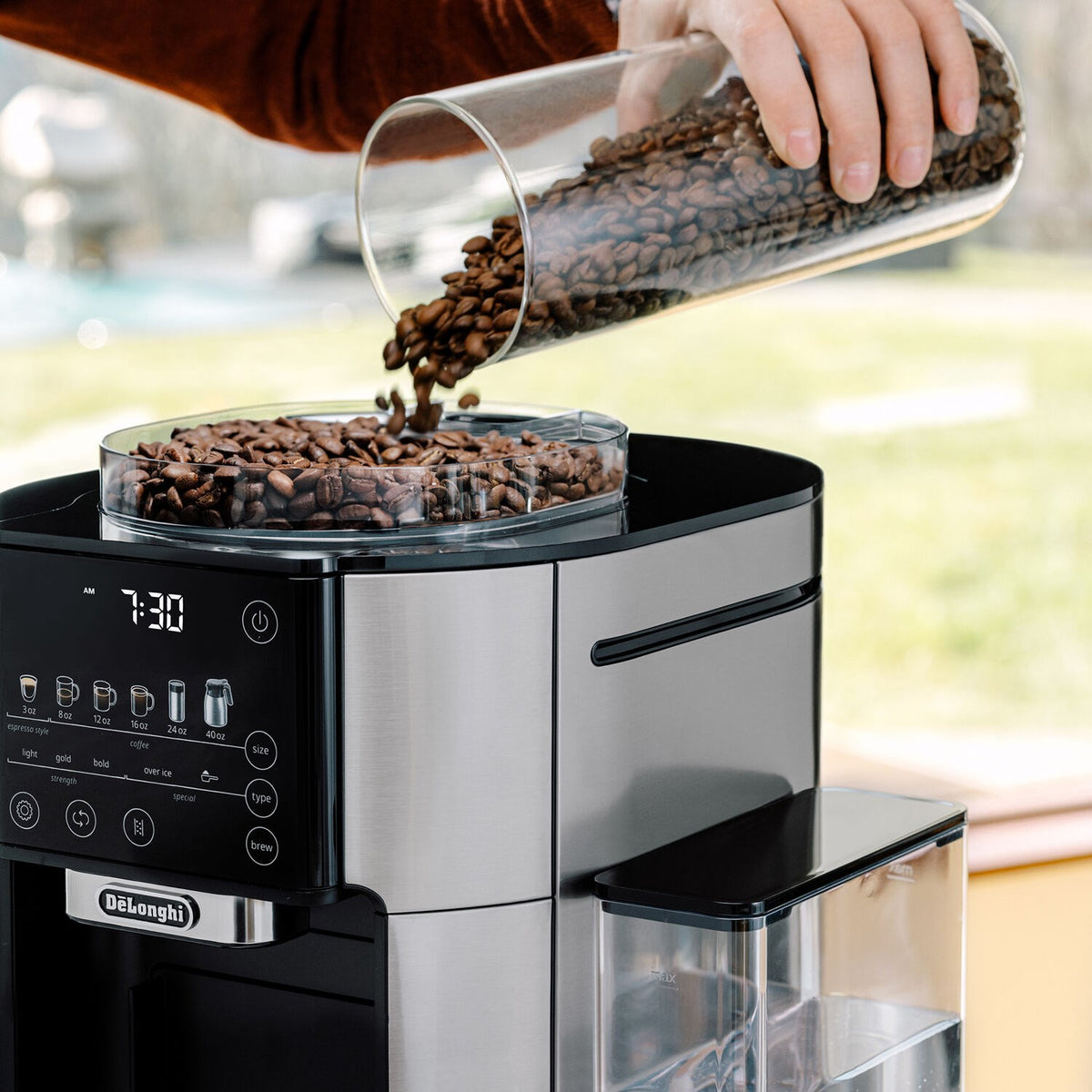 De'Longhi TrueBrew coffee maker with glass bean hopper, showing coffee beans being poured in