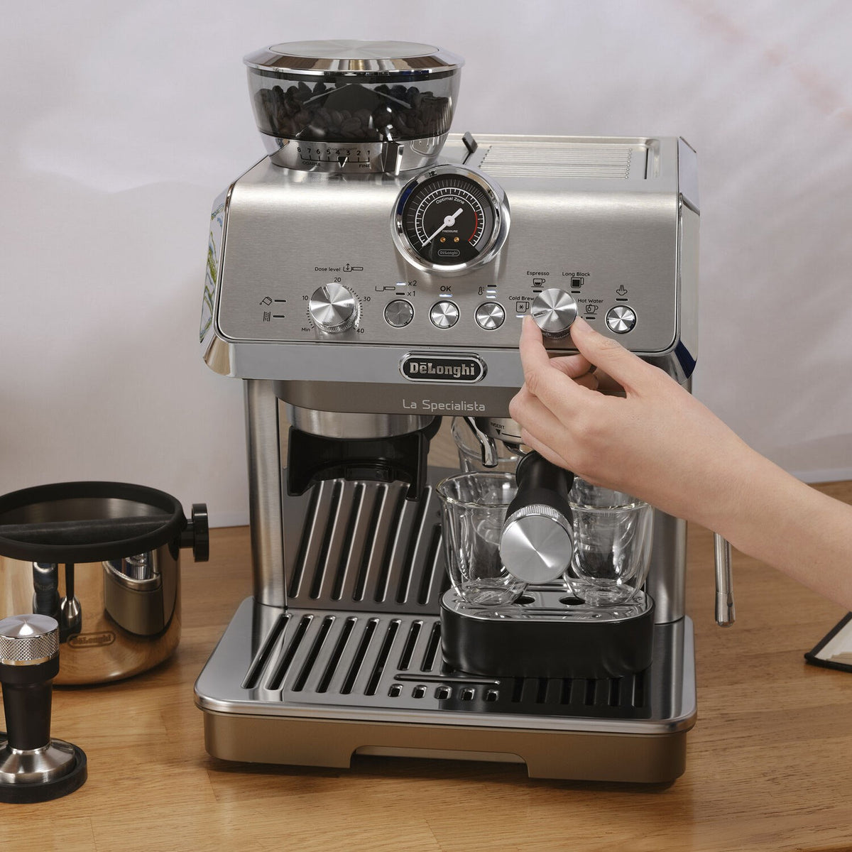 Silver espresso machine with steam wand and frothing pitcher held near brewing area