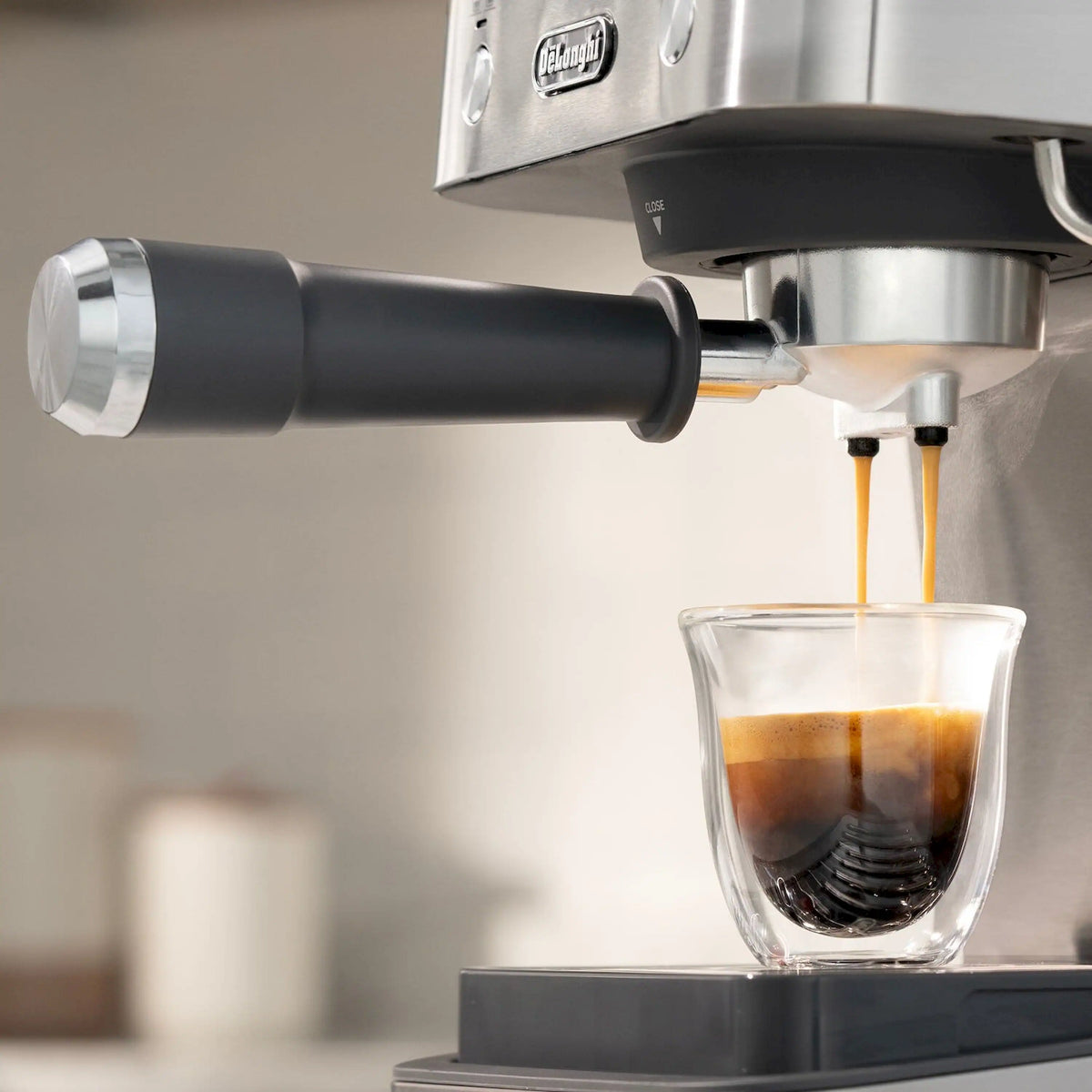 Milk frother nozzle pouring espresso into a clear glass under the spout.
