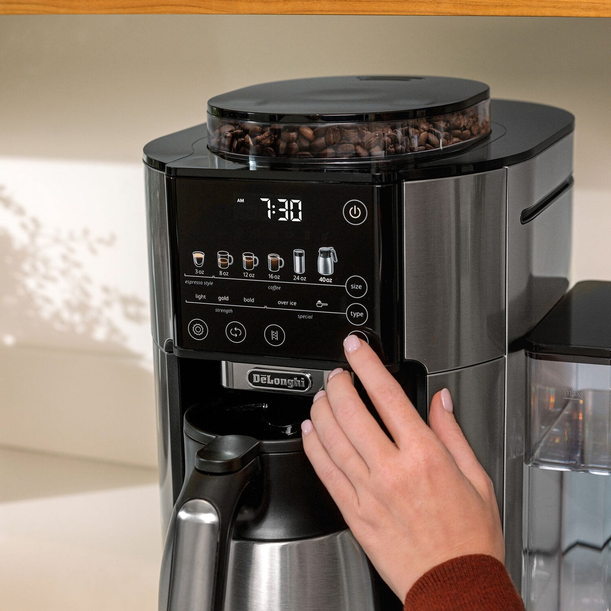 De'Longhi TrueBrew coffee maker with touchscreen panel and hand pressing a button on display
