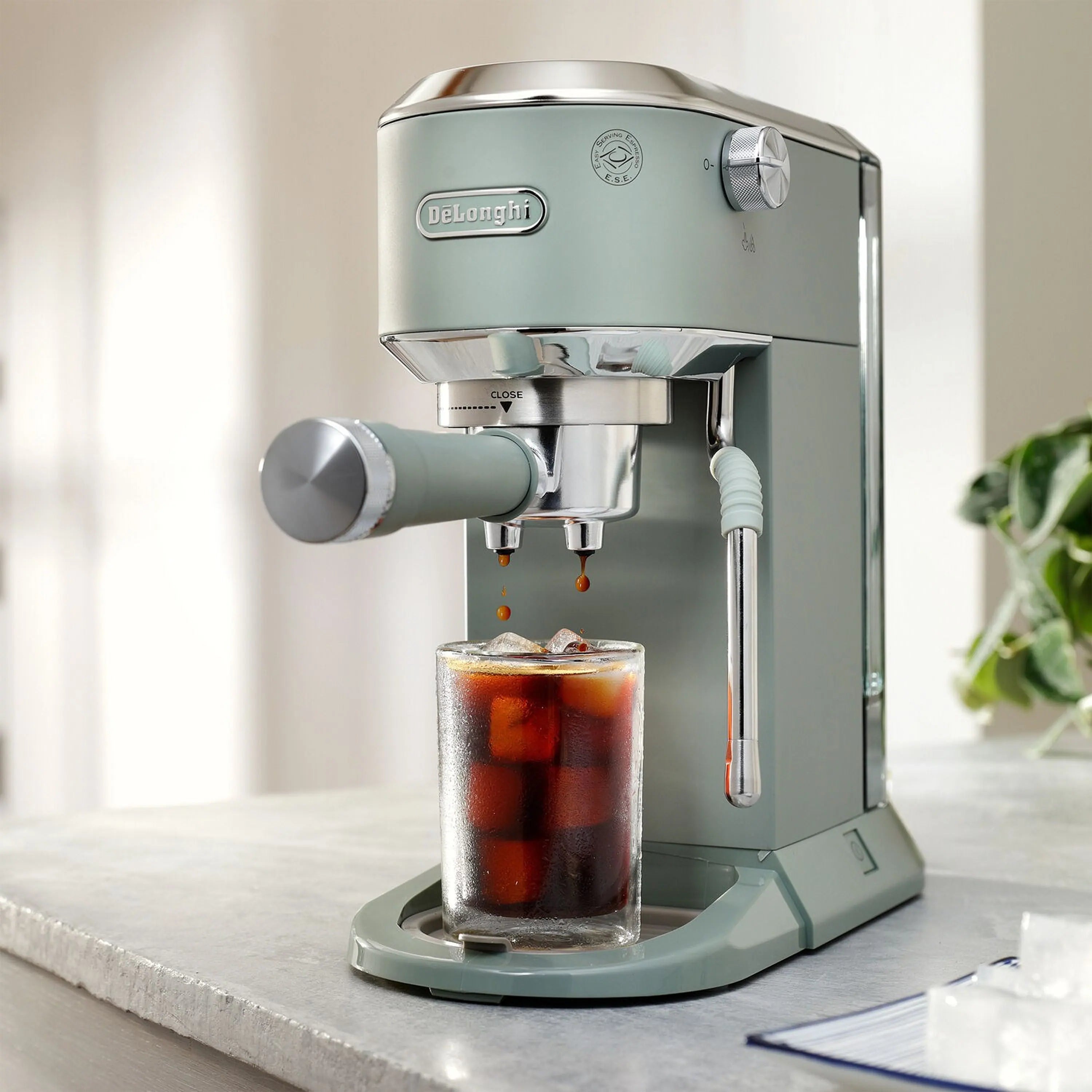 Green De'Longhi pump espresso machine with frothing wand and tall glass on base tray