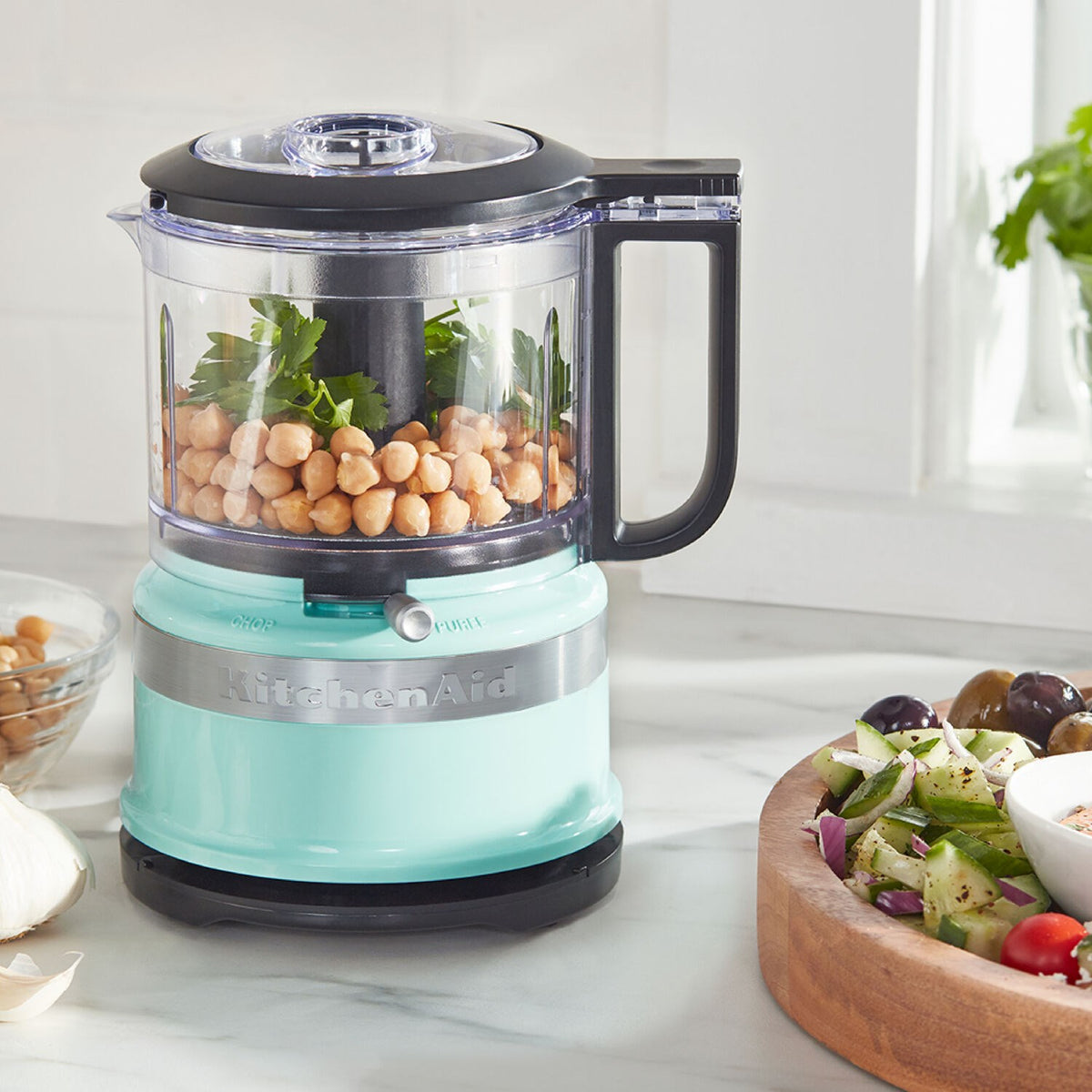 KitchenAid food chopper with ice-blue base, clear bowl filled, black lid and handle