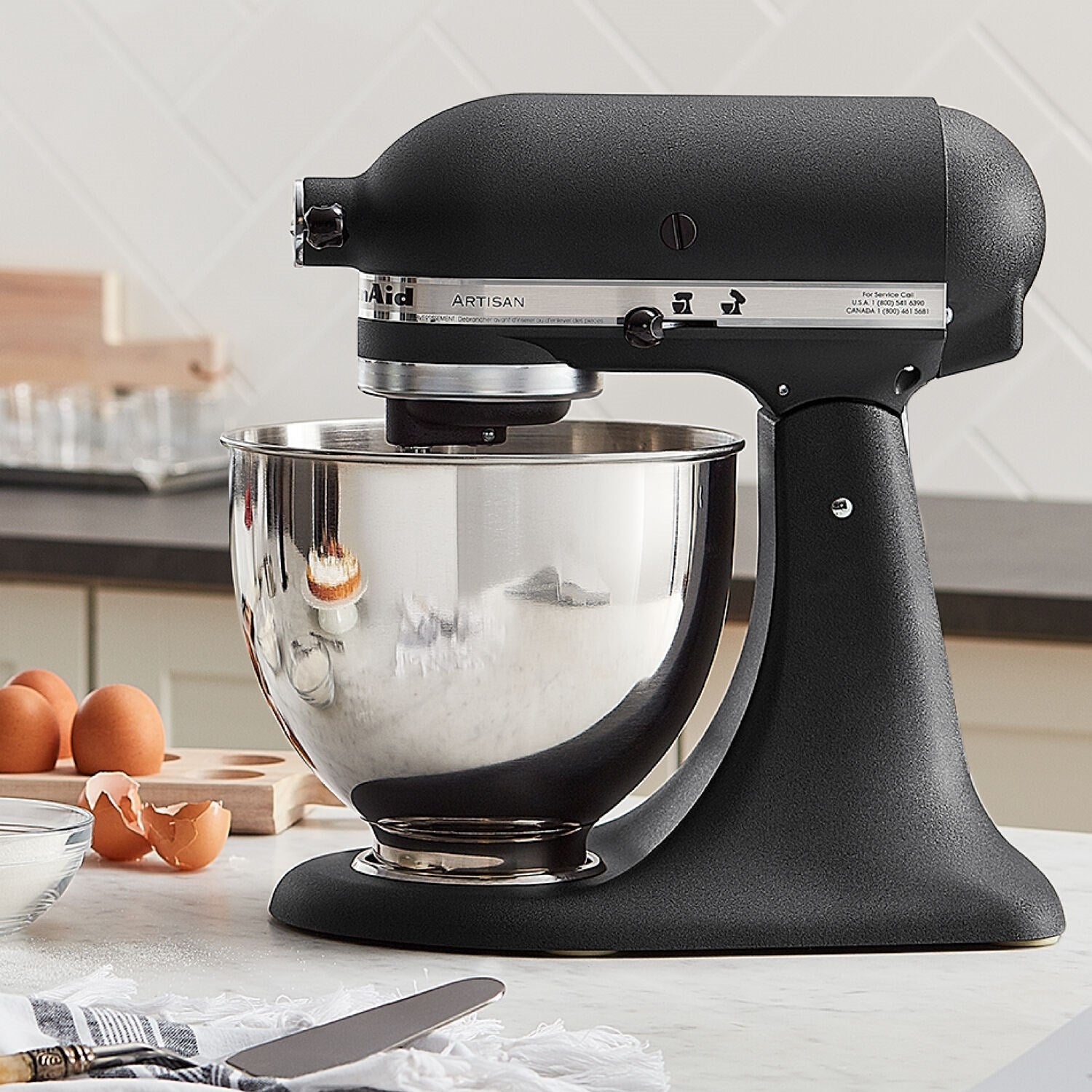 Black tilt-head stand mixer with stainless bowl, side view, beaters visible