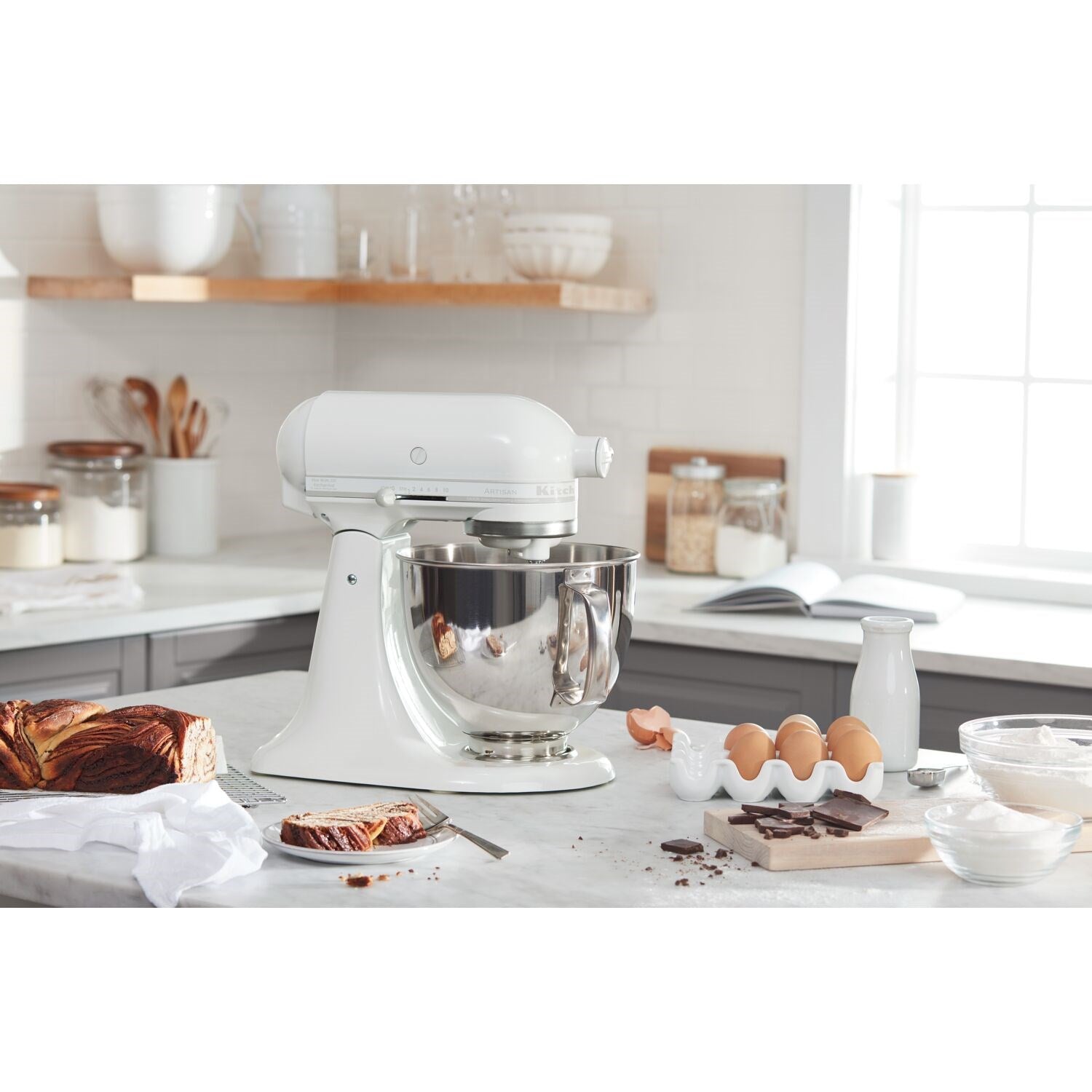 White tilt-head stand mixer with stainless bowl and whisk attachment on kitchen counter.