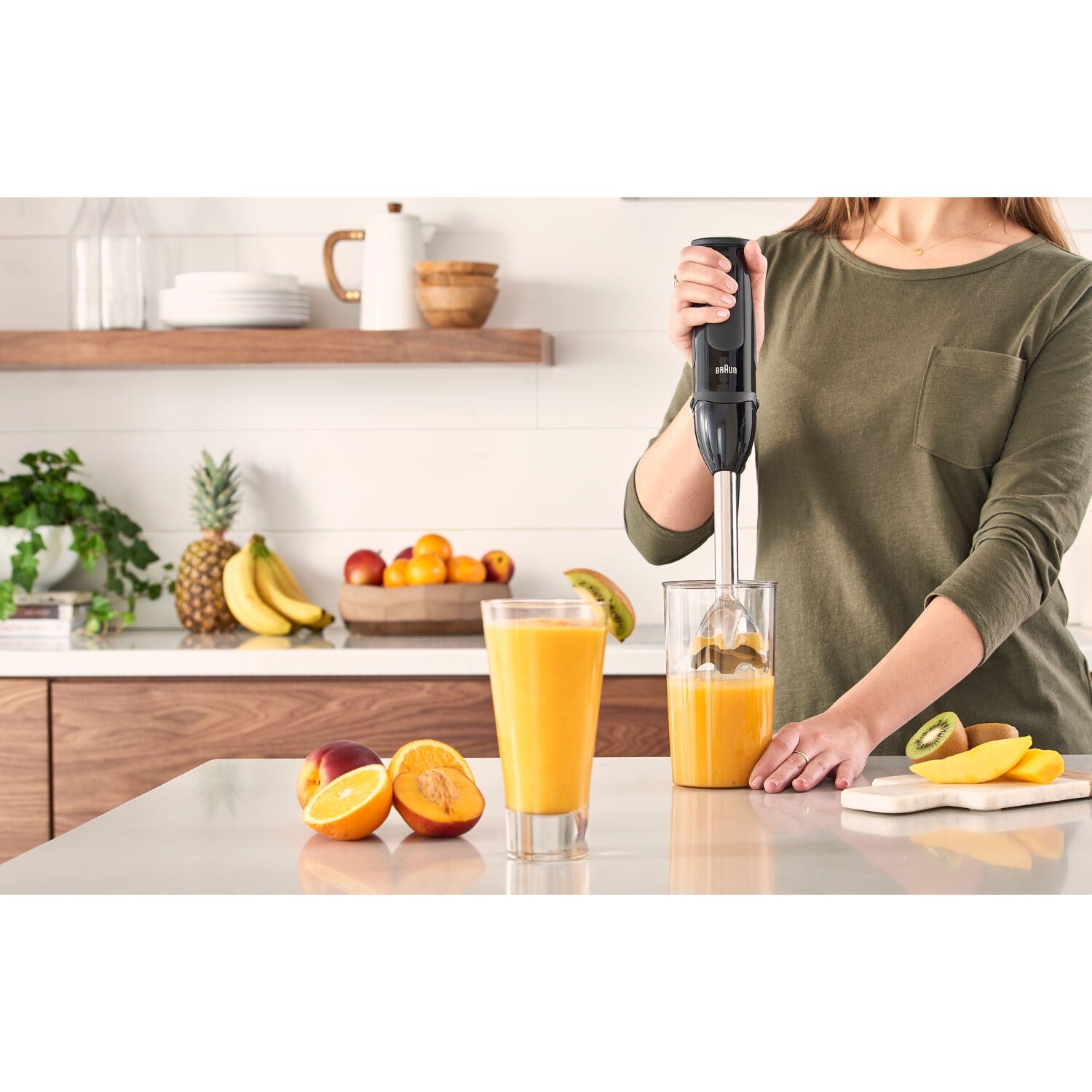 Hand blender in dark housing blending orange drink in a clear cup