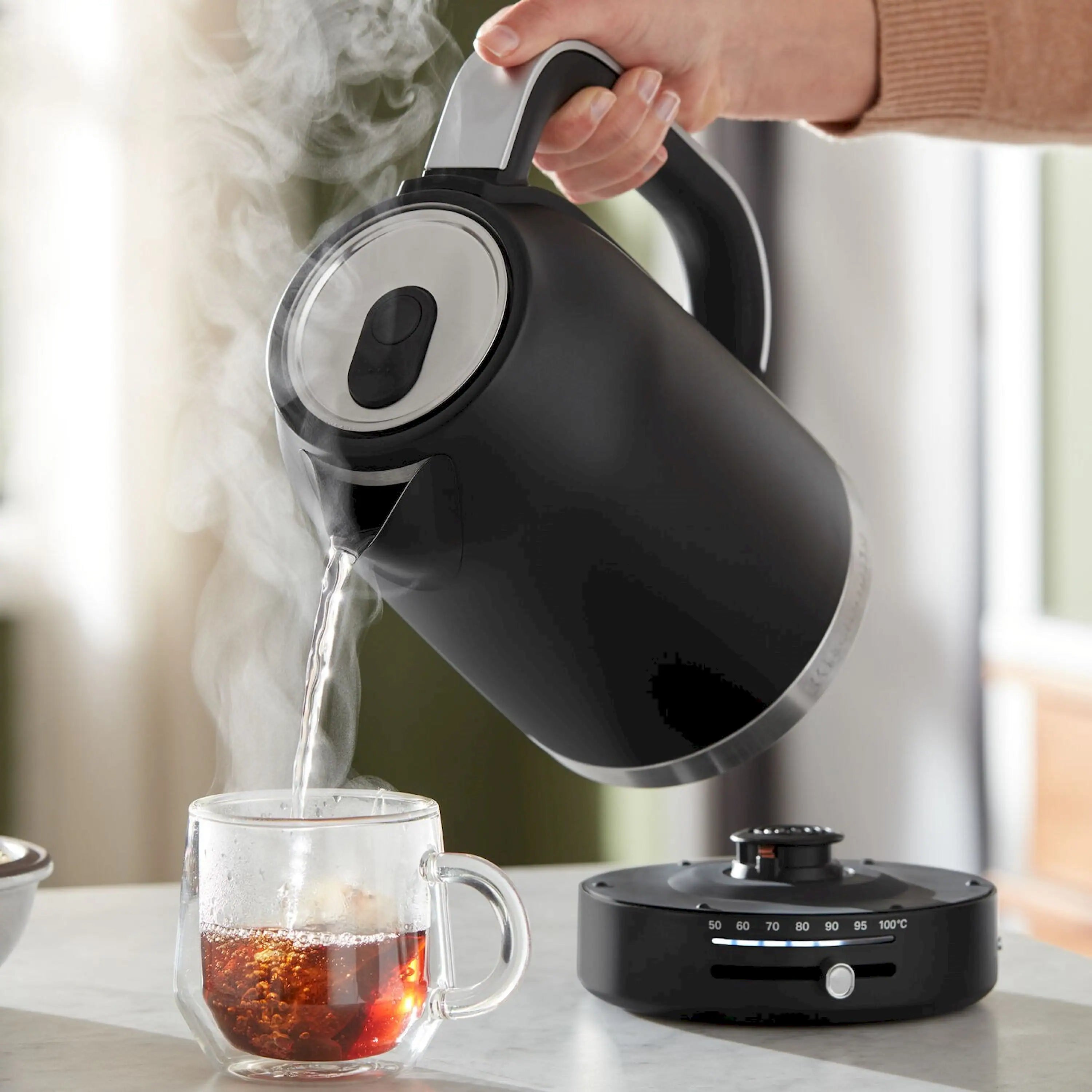 Matte black electric kettle pouring hot water from spout into glass cup