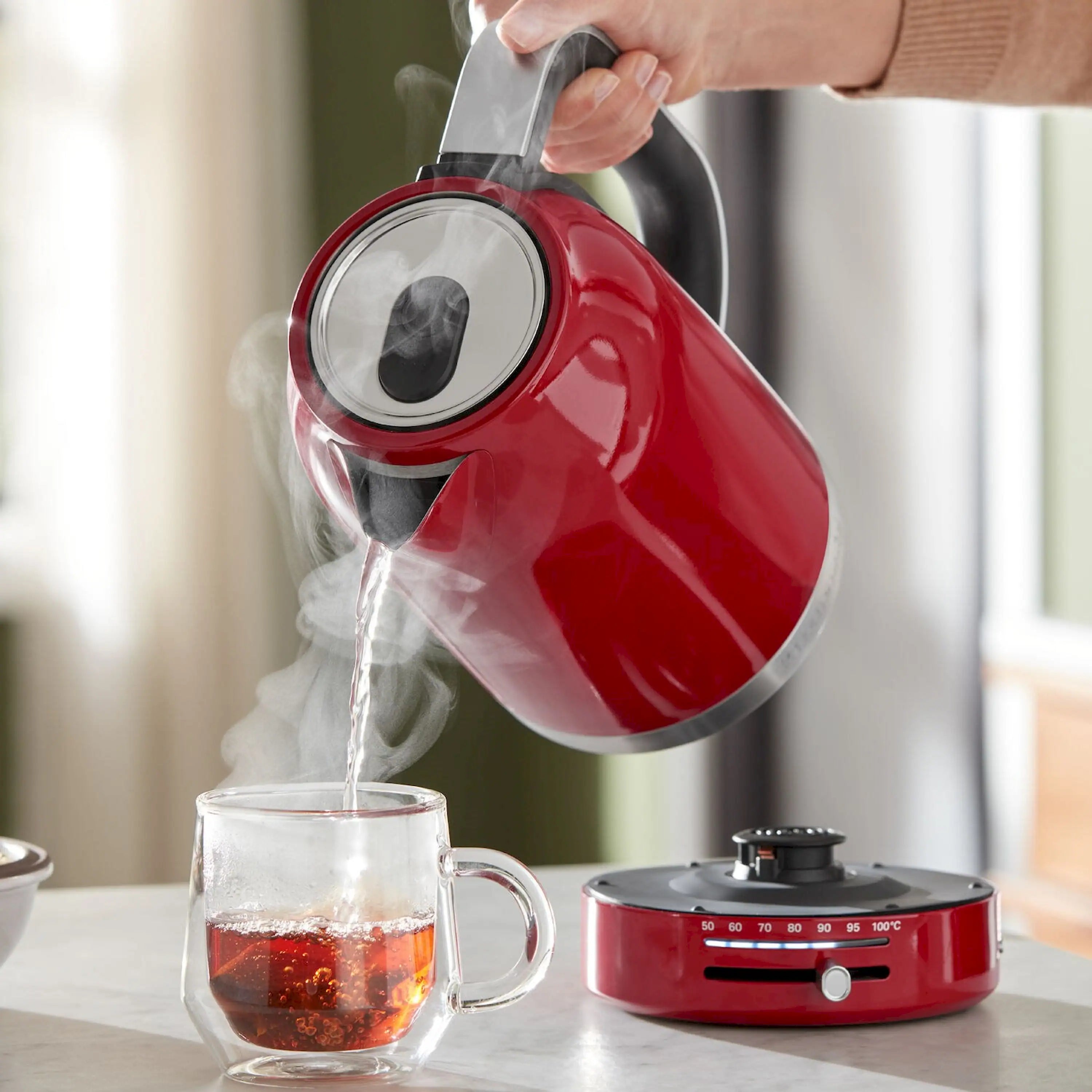Red electric water kettle pouring hot water into a clear cup; black handle
