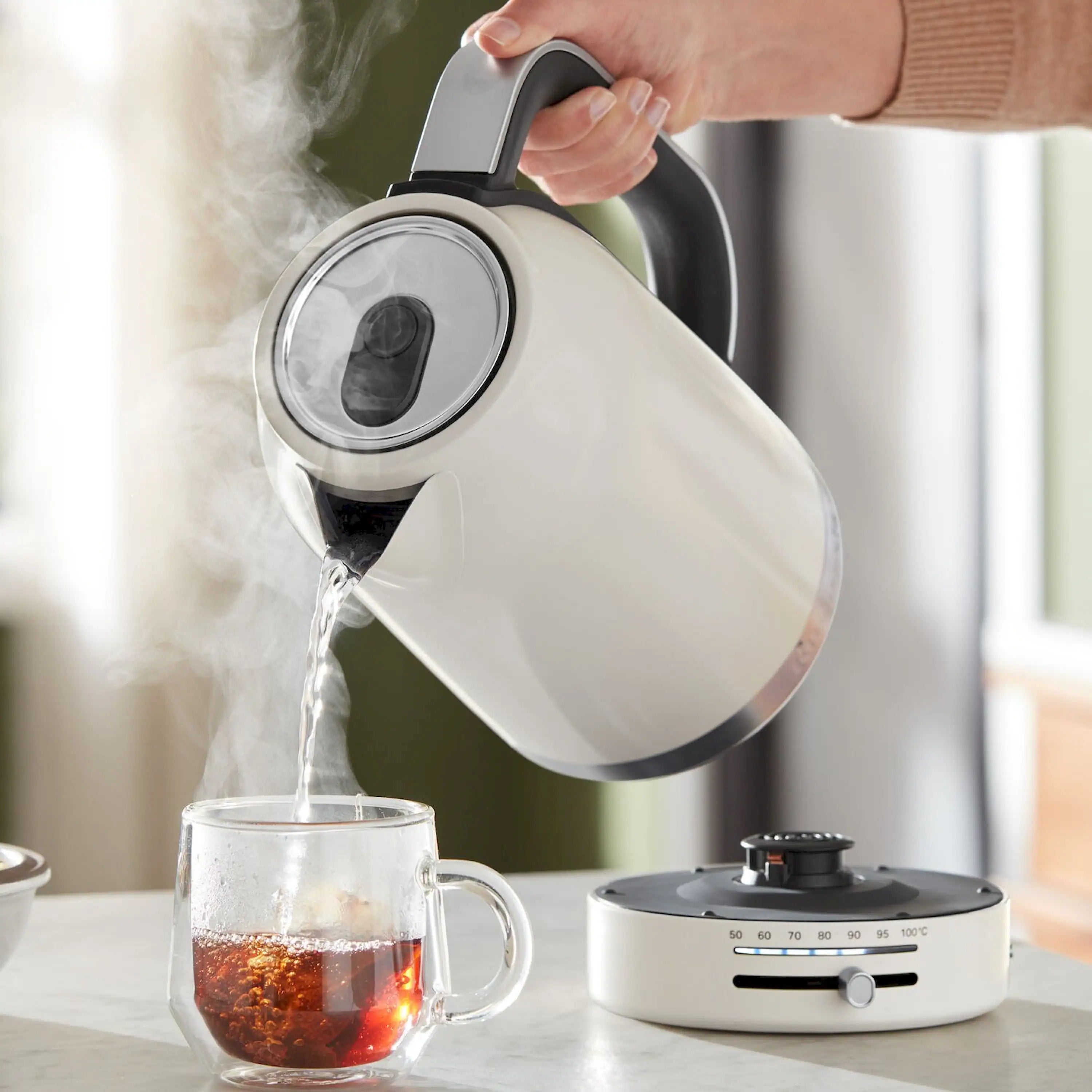 Porcelain electric kettle pouring hot water into glass cup, black spout handle